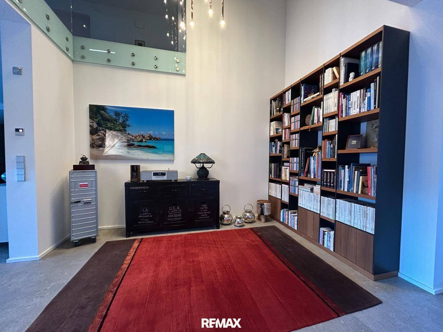 Geräumiger Wohnbereich mit hoher Decke, großer Bücherwand und modernem Teppich.