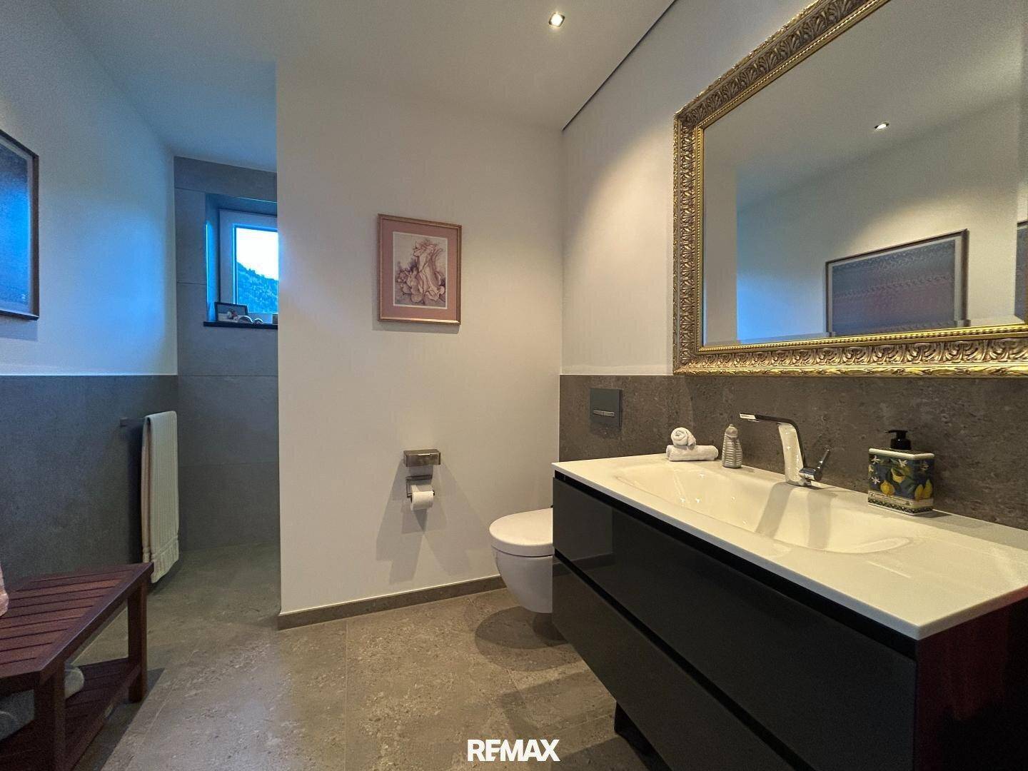 Modernes Badezimmer mit Waschtisch, Wand-WC und eleganten Fliesen an den Wänden.