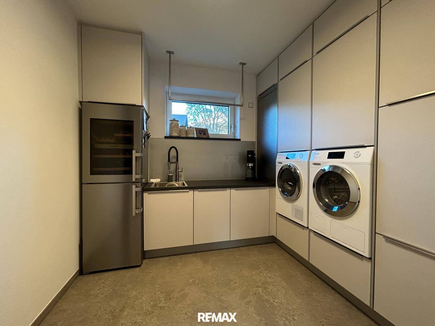 Praktischer Hauswirtschaftsraum mit Waschmaschine, Trockner, Spülbecken und Weinkühlschrank.