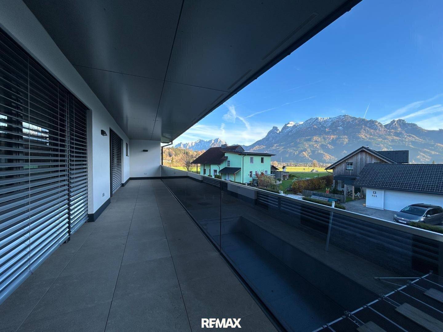 Geräumiger Balkon mit Glasbrüstung und atemberaubendem Bergblick unter blauem Himmel.