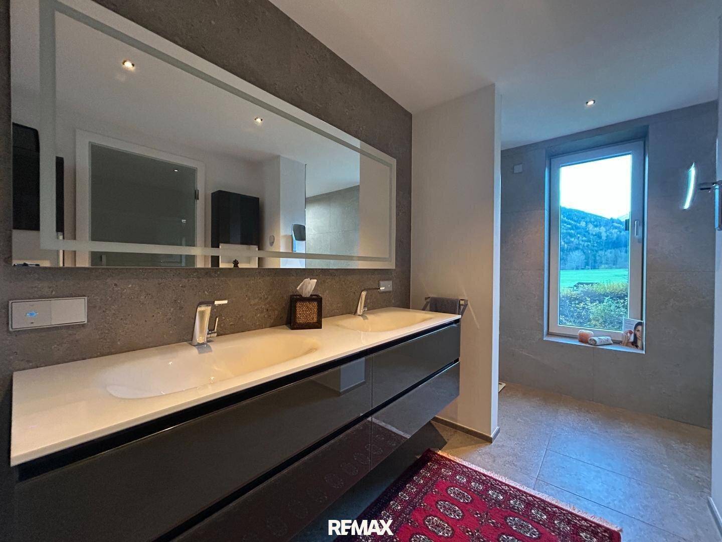 Luxuriöses Badezimmer mit Doppelwaschtisch, großem Spiegel und eleganten Fliesen.