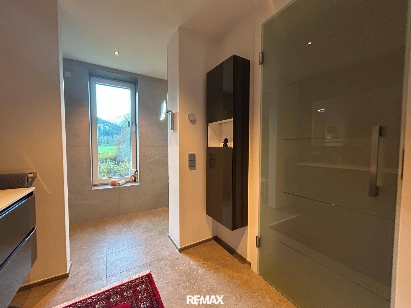 Modernes Badezimmer mit großformatigen Fliesen, Fenster und Blick auf die umliegende Natur.