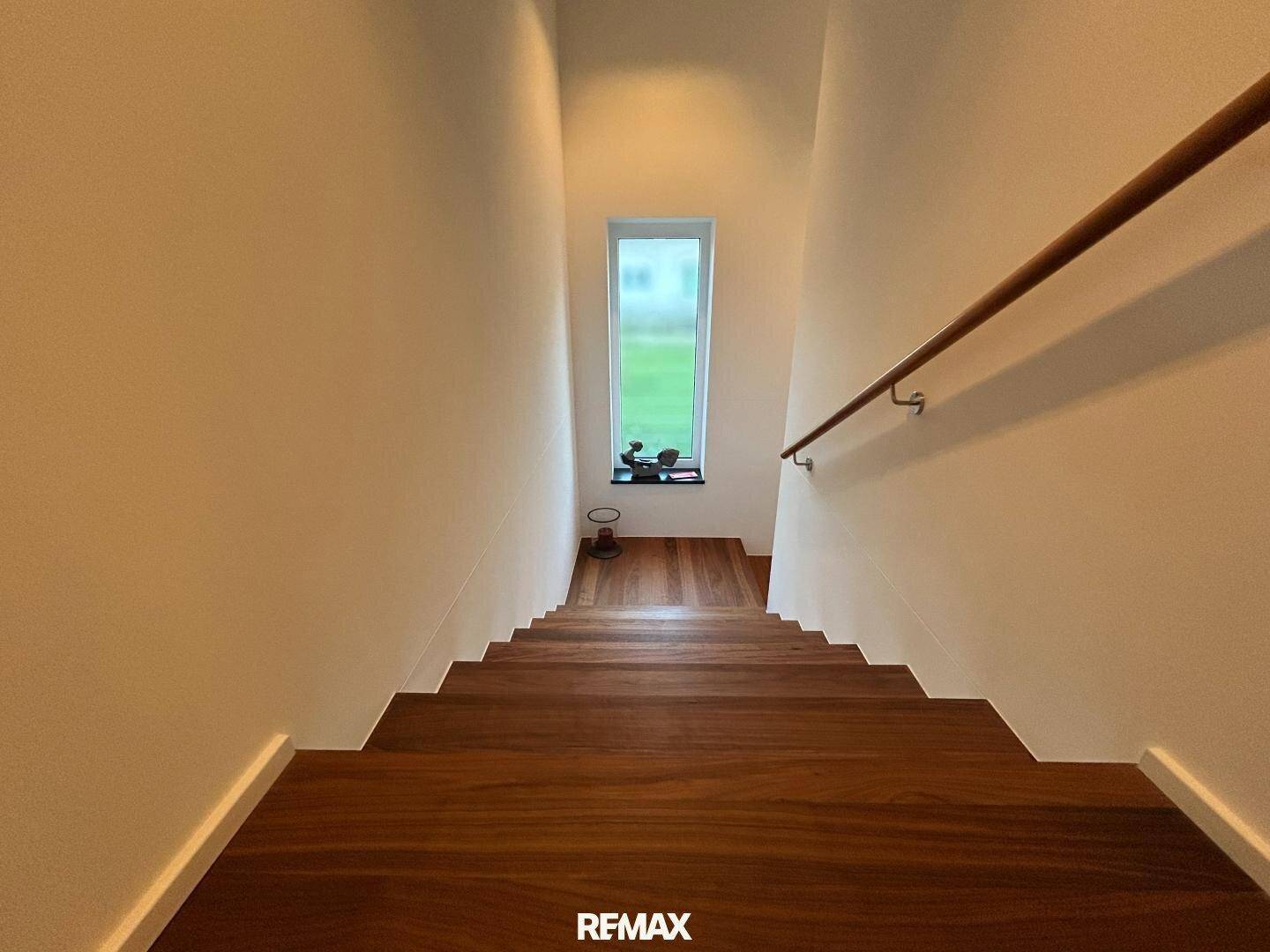 Elegante Holztreppe führt nach unten, mit einem Fenster am Treppenabsatz.