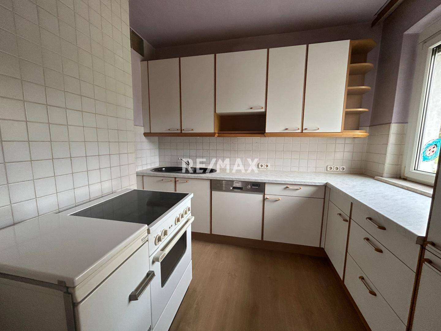 Küche mit weißen Einbauschränken, Spülmaschine und einem älteren Elektroherd, der Renovierung benötigt.