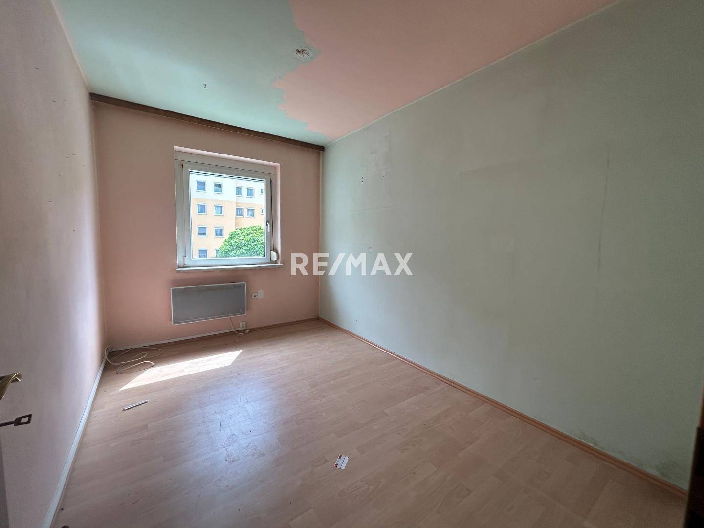 Leeres Zimmer mit hellem Laminatboden und einem Fenster, das Tageslicht hereinlässt.