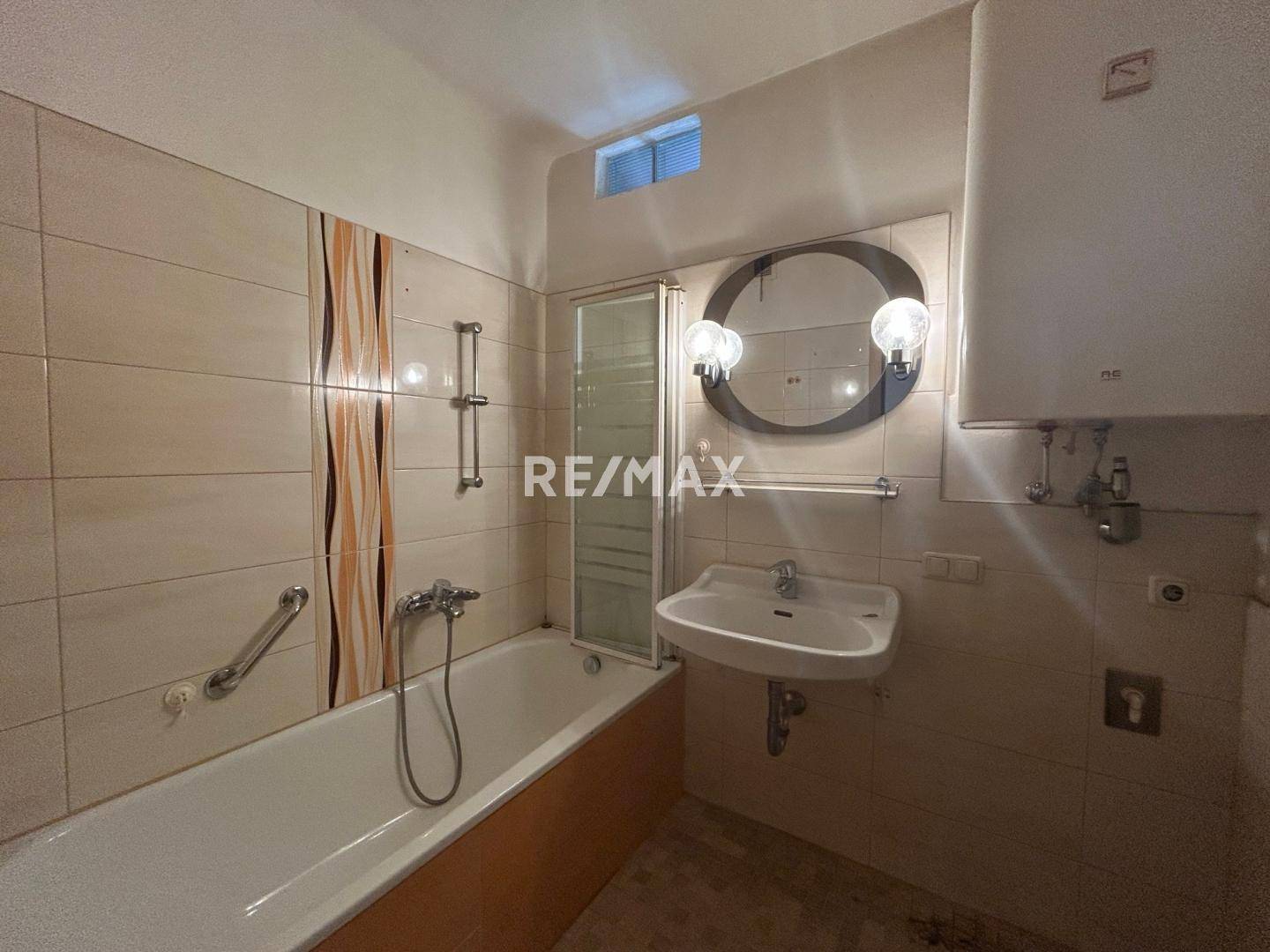 Badezimmer mit Badewanne, Waschbecken und Fliesen in warmen Farbtönen, ausgestattet mit Haltegriffen.