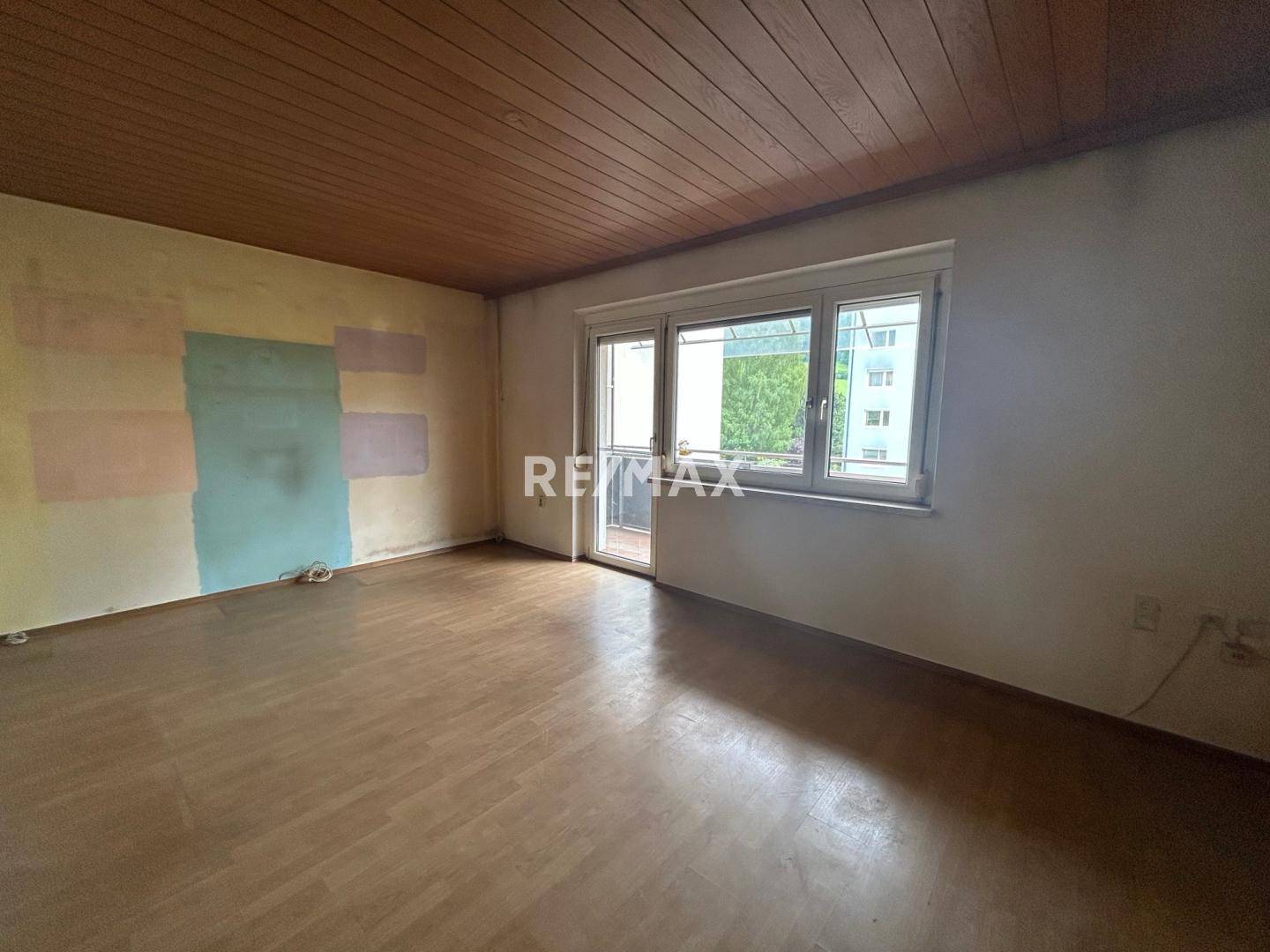 Geräumiges Zimmer mit Holzboden und Zugang zu einem Balkon, die Wände zeigen Renovierungsbedarf.