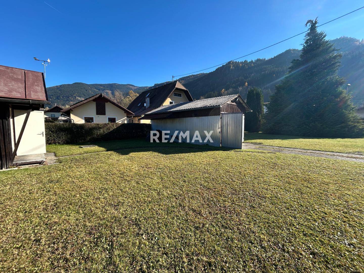 Gartenansicht mit Rasenfläche, einer Garage und weiteren Gebäuden im ländlichen Umfeld.