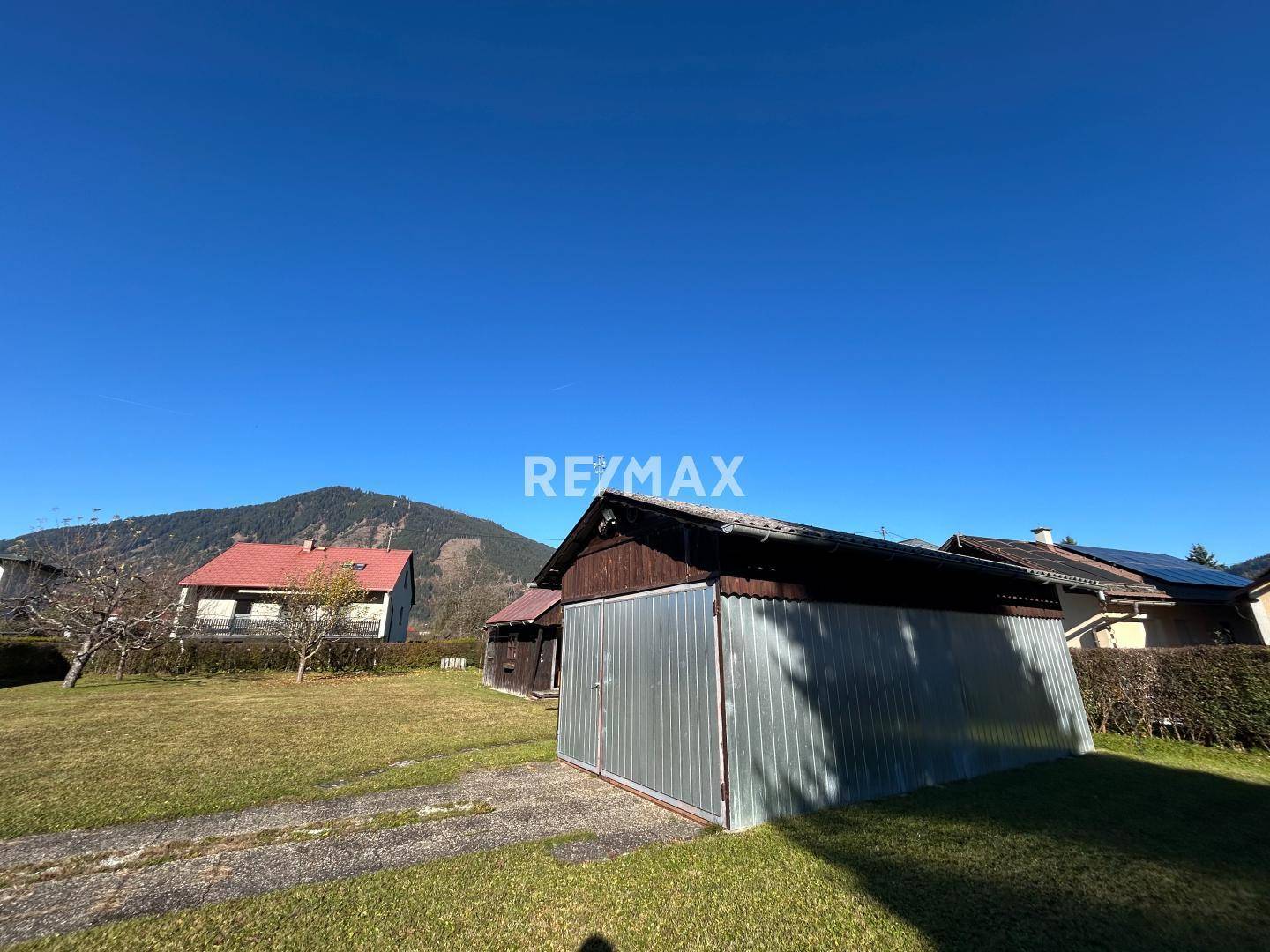 Garten mit Rasenfläche und einer einfachen Garage, umgeben von ländlicher Berglandschaft.