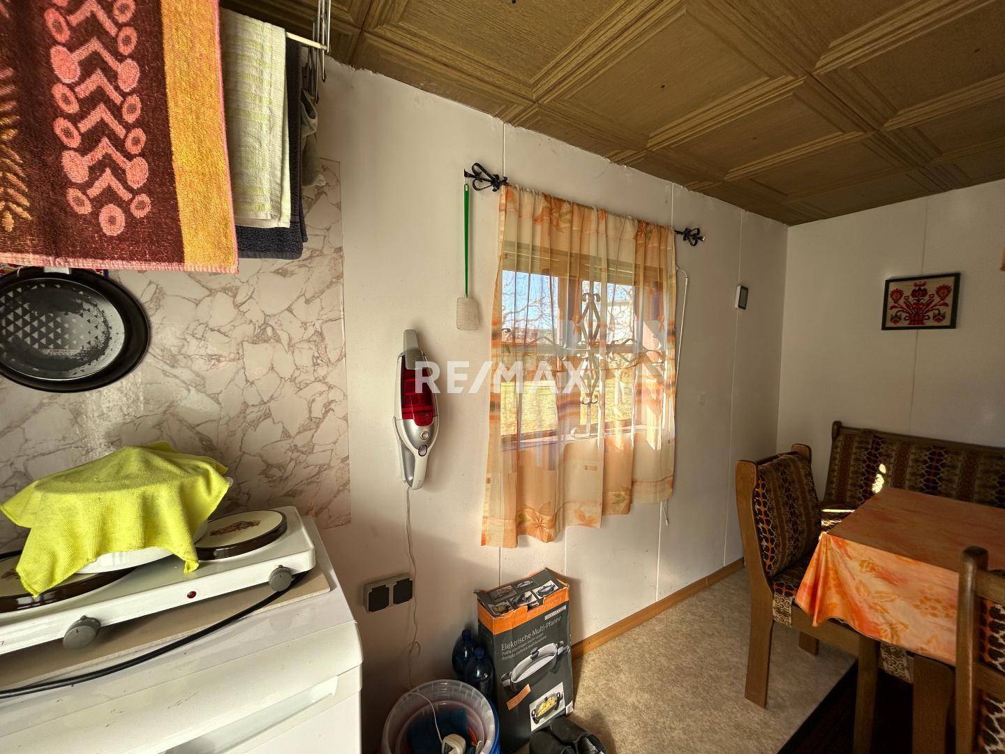 Kleiner, einfach eingerichteter Raum mit Fenster, Tisch und Stühlen, möglicherweise eine provisorische Küche.