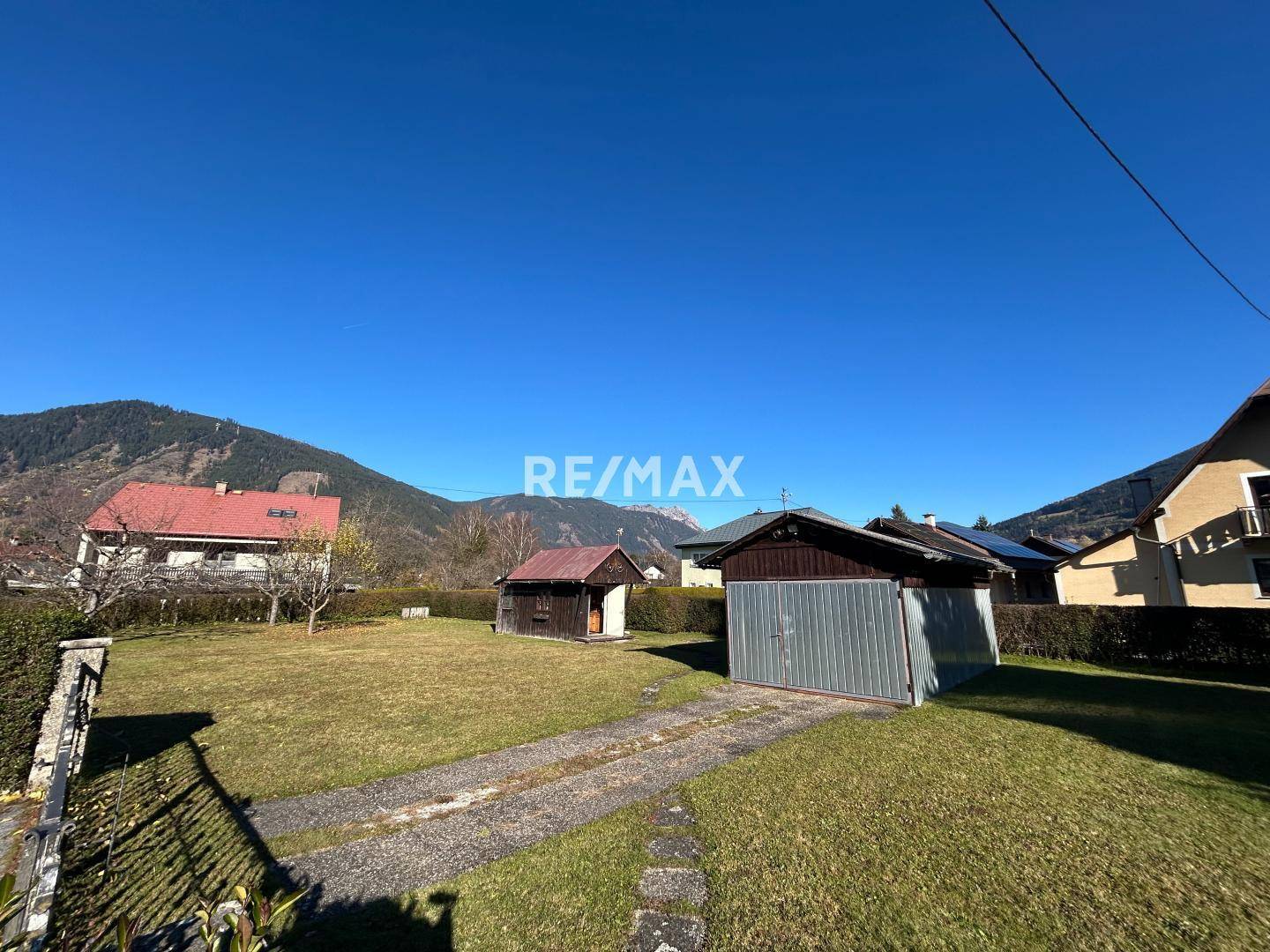 Panoramablick über den Garten mit Garage und der beeindruckenden Bergkulisse im Hintergrund.