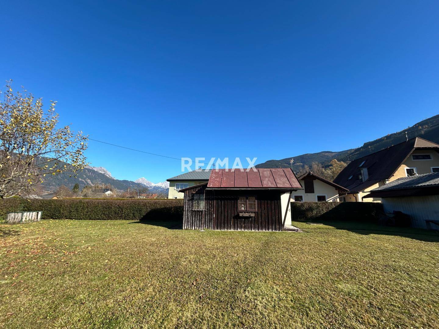 Weitläufiger Garten mit Rasen, einem kleinen Holzschuppen und Bergblick im Hintergrund.
