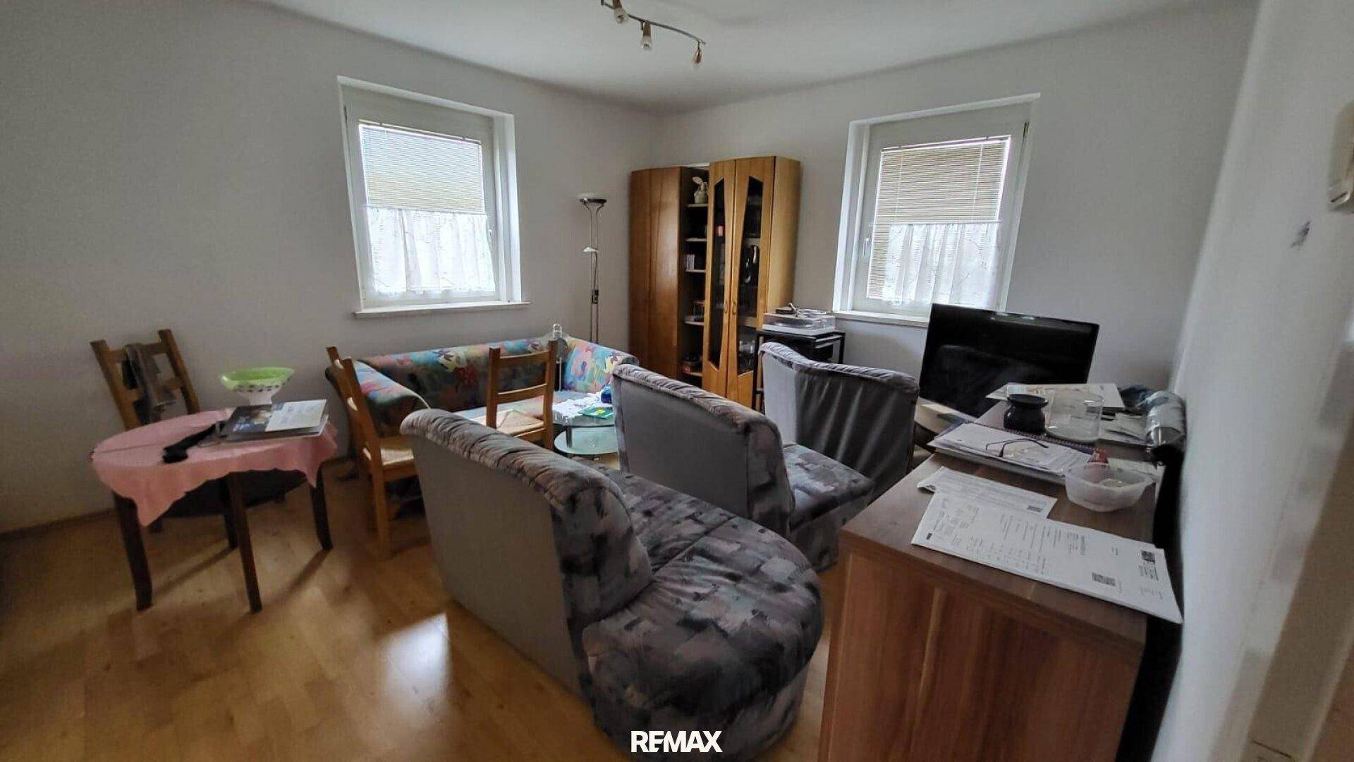 Gemütliches Wohnzimmer mit Holzfußboden, zwei Fenstern und bequemen Sofas.