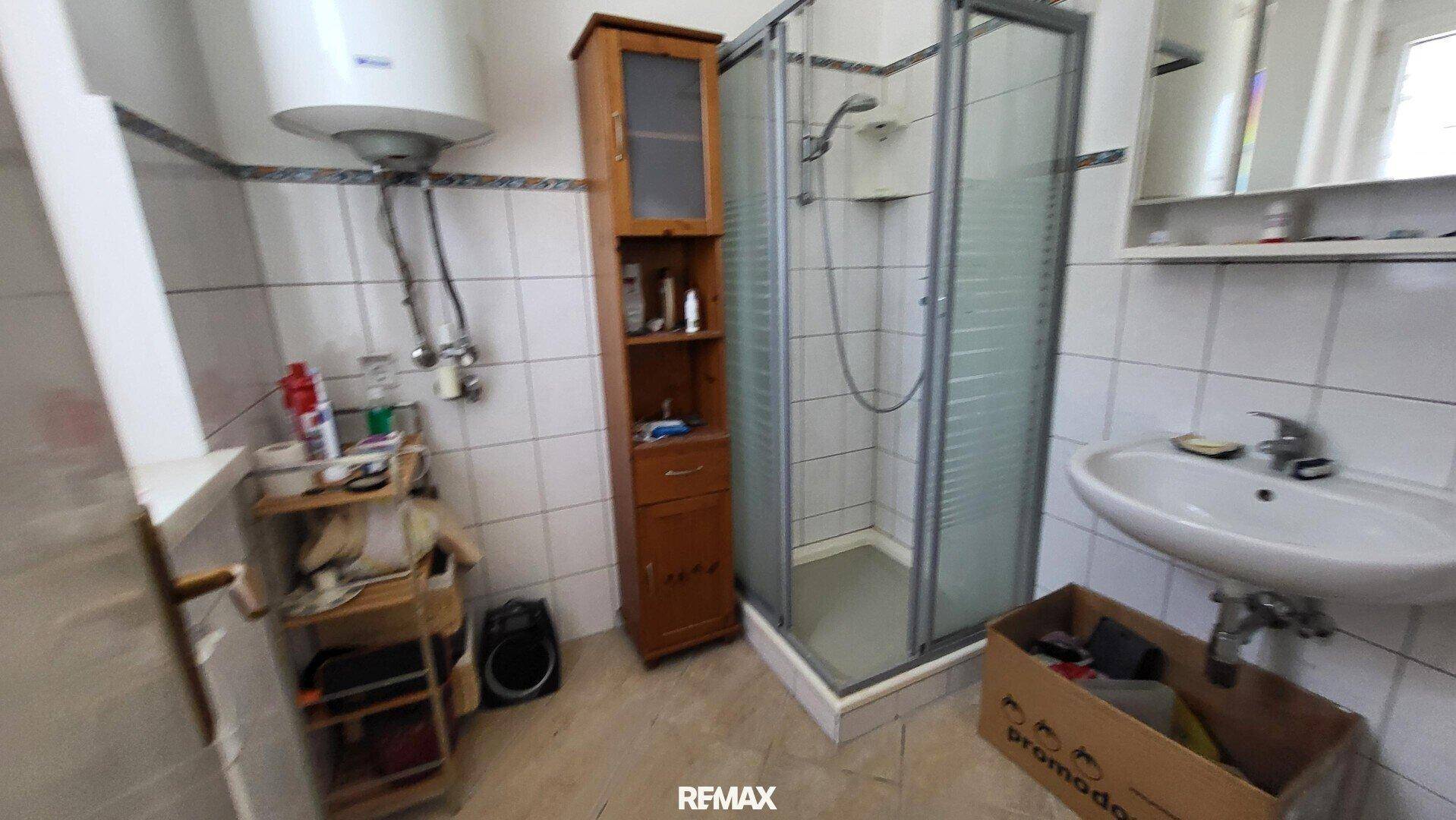 Badezimmer mit Duschkabine, Boiler und Fliesen an Wänden und Boden.