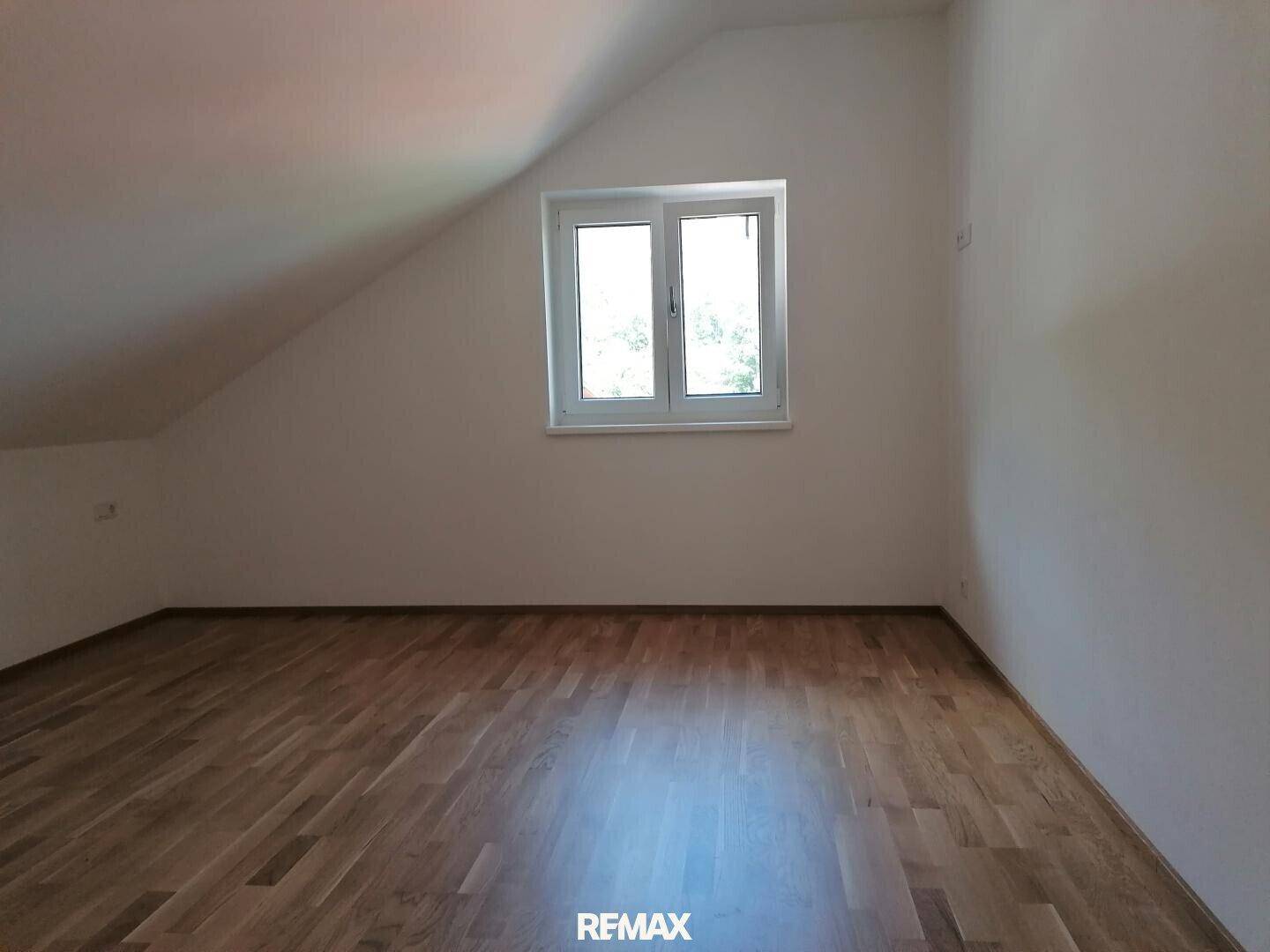 Schlafzimmer im Dachgeschoss mit Parkettboden, Fenster und schräger Decke.
