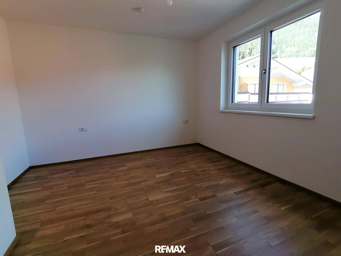 Leeres Schlafzimmer mit Parkettboden und Fenster, das viel Tageslicht hereinlässt.
