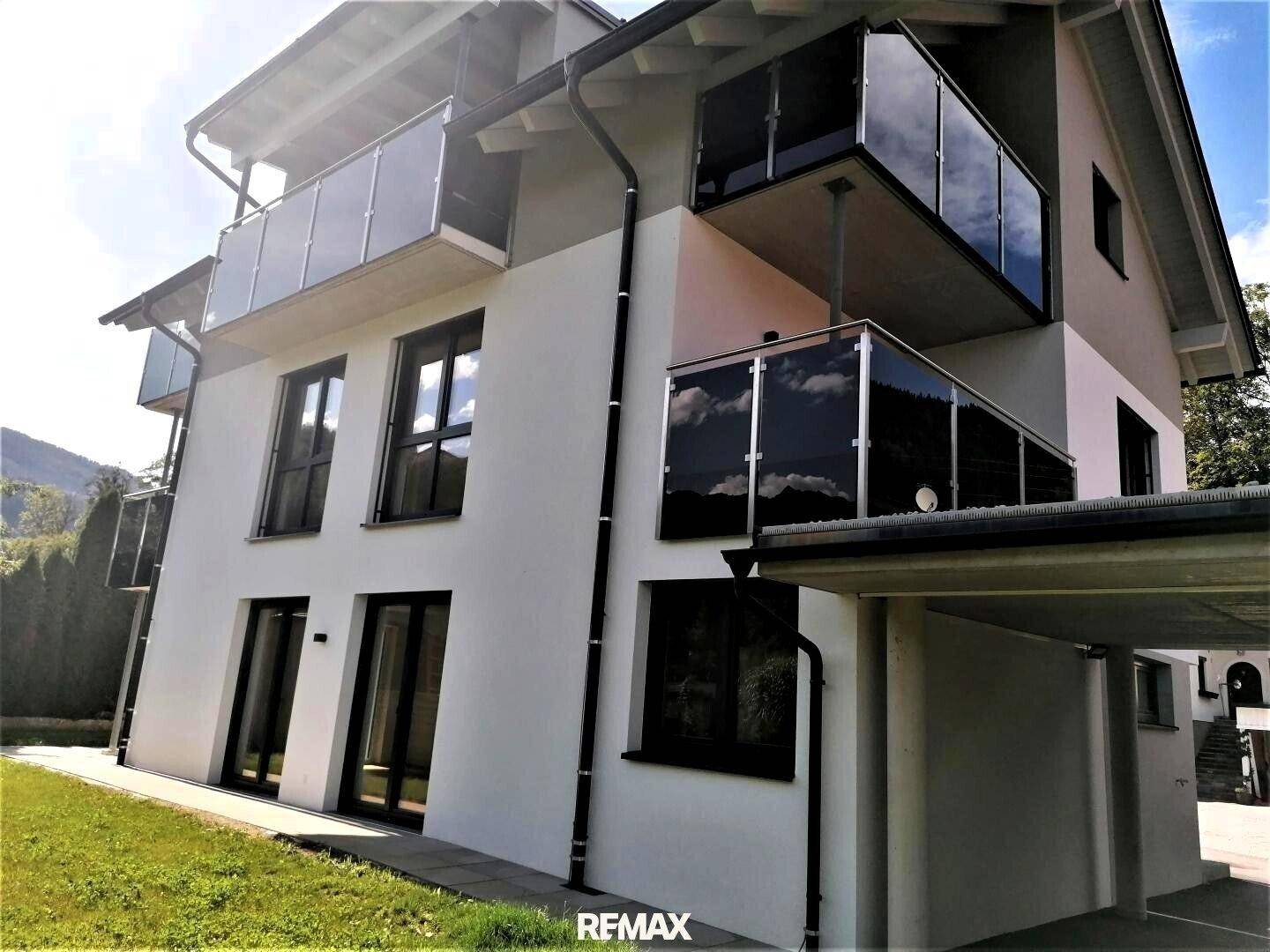 Moderne Gebäudefassade mit Balkonen und einem überdachten Carport im Vordergrund.