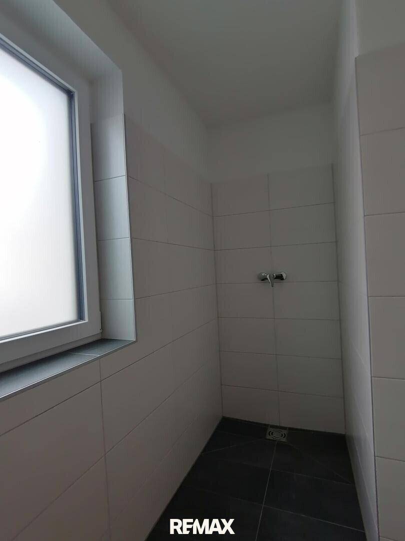 Geräumiger Duschbereich mit Fliesenboden und Fenster, ideal für eine begehbare Dusche.