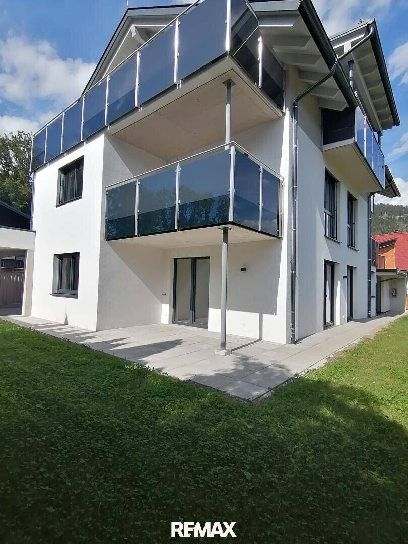 Moderne Gebäudefassade mit mehreren Balkonen und einer gepflasterten Terrasse im Erdgeschoss.