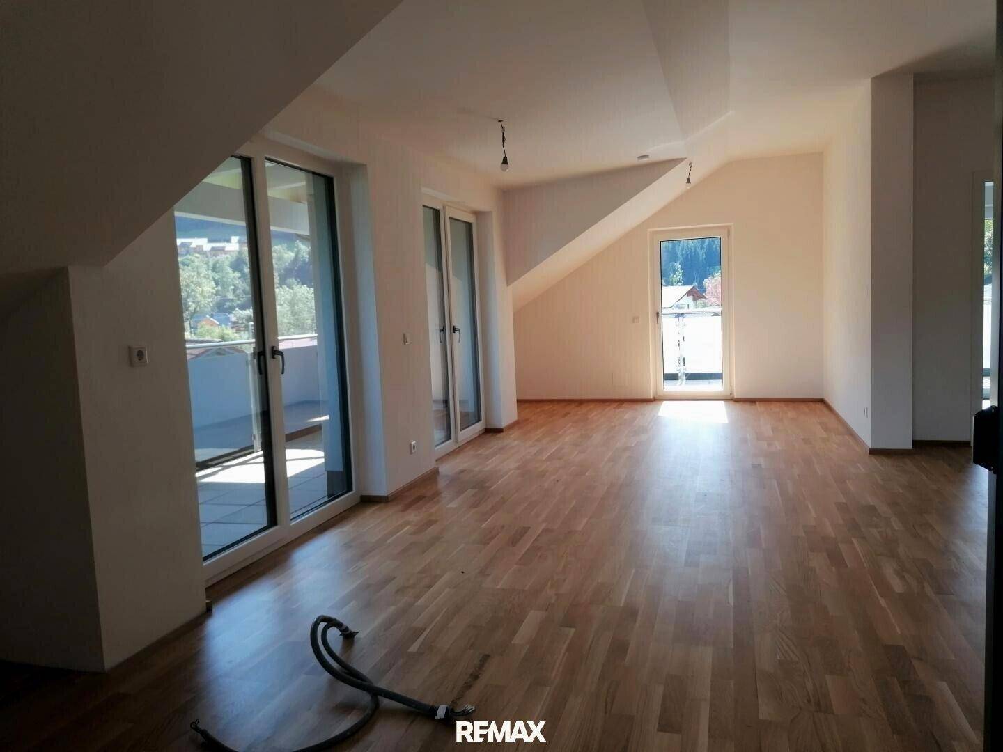 Lichtdurchfluteter Wohnbereich im Dachgeschoss mit Parkettboden und Zugang zu einem Balkon.