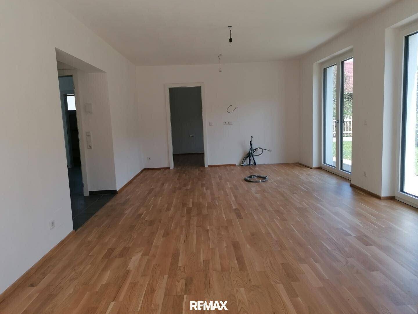 Helles, leeres Wohnzimmer mit Parkettboden und großen Fenstern zum Garten.