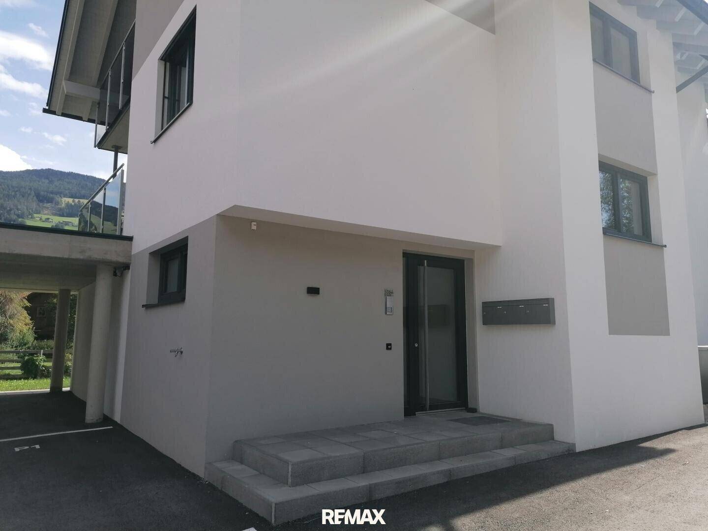 Eingangsbereich eines modernen Gebäudes mit Treppen, Haustür und einem Briefkasten an der Fassade.