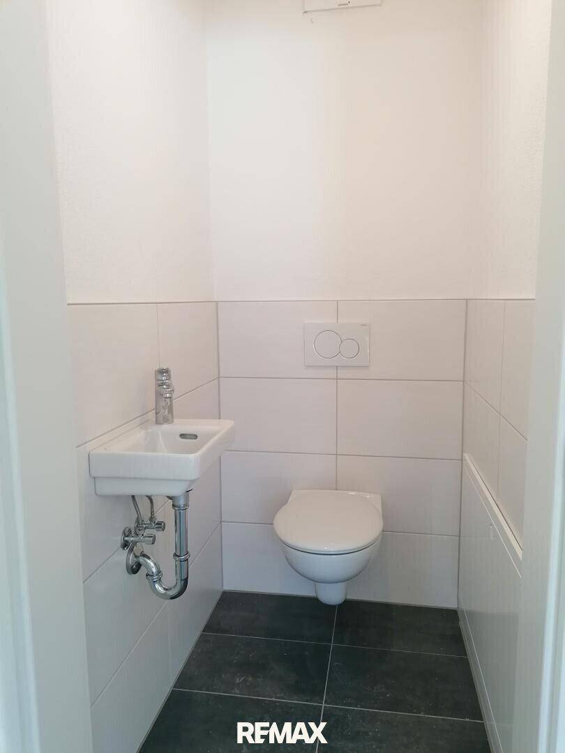 Modernes Gäste-WC mit wandhängendem WC, kleinem Waschbecken und dunklen Bodenfliesen.