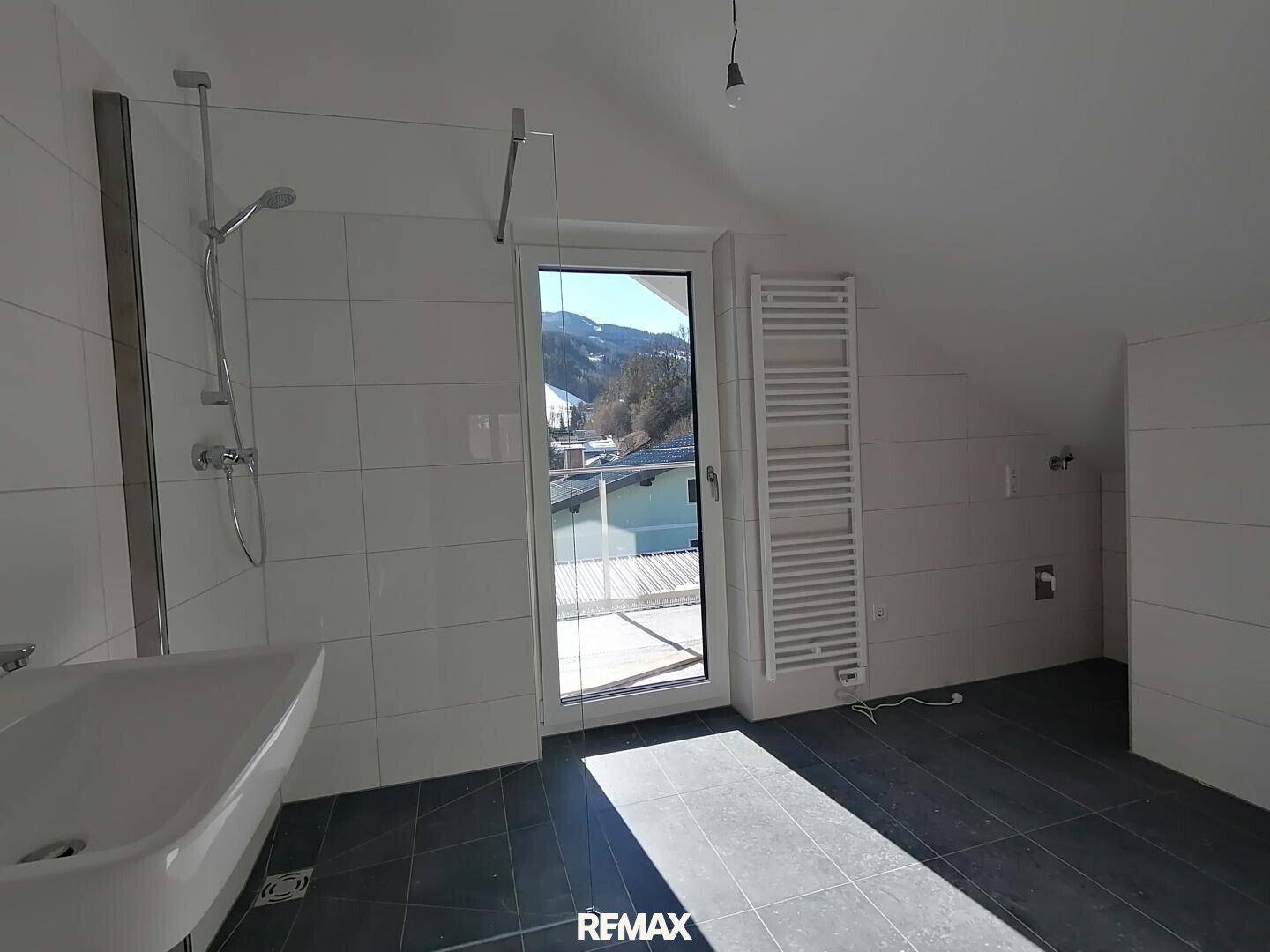 Geräumiges Badezimmer im Dachgeschoss mit Dusche, Waschbecken und Zugang zum Balkon.