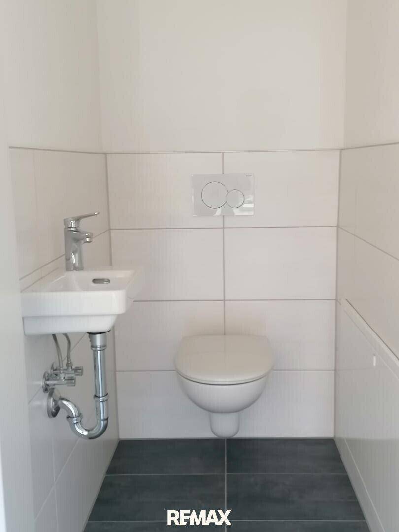 Modernes Gäste-WC mit Wand-WC, kleinem Waschbecken und weißen Fliesen.