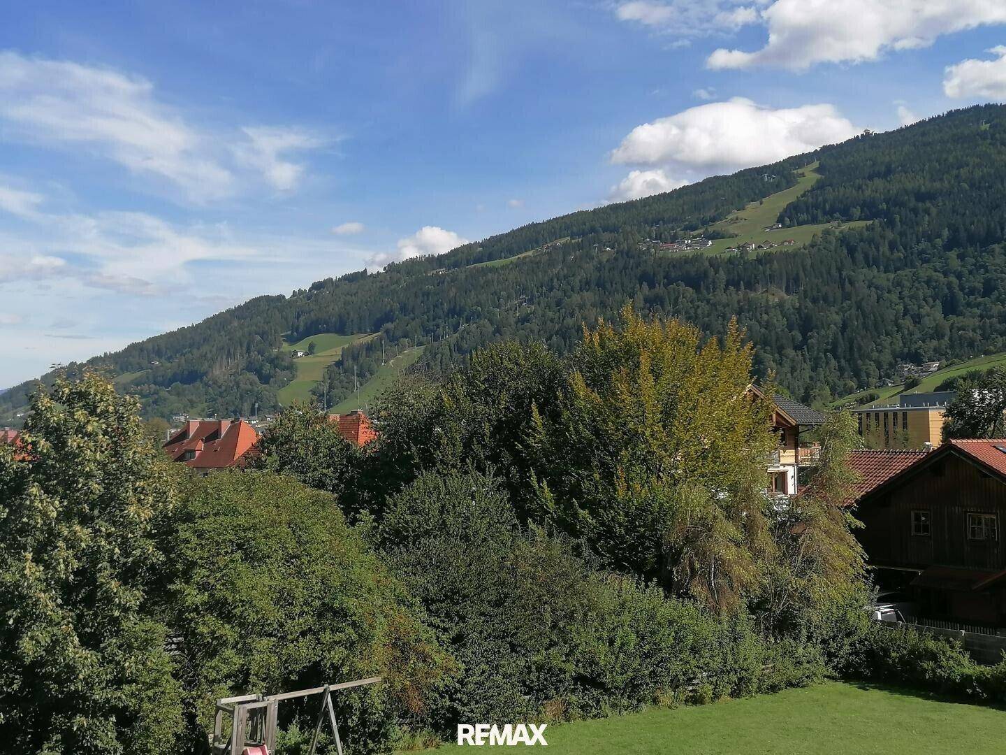 Weitläufiger Blick auf bewaldete Berghänge und grüne Landschaft mit einem Spielplatz im Vordergrund.