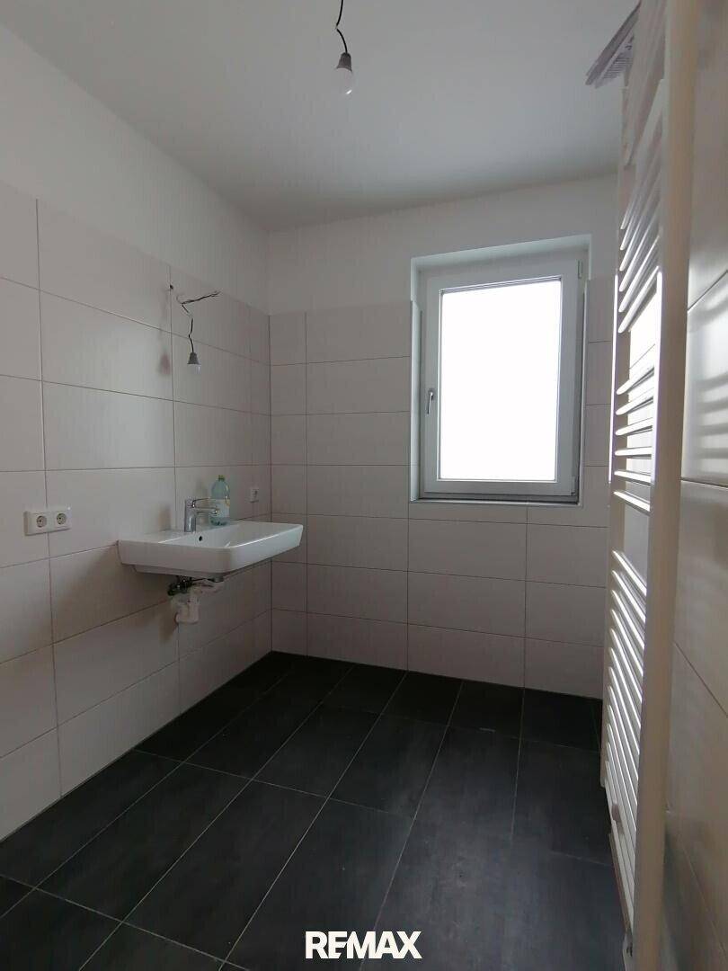 Helles Badezimmer mit Waschbecken, Fenster und beheiztem Handtuchhalter, bereit für die Einrichtung.