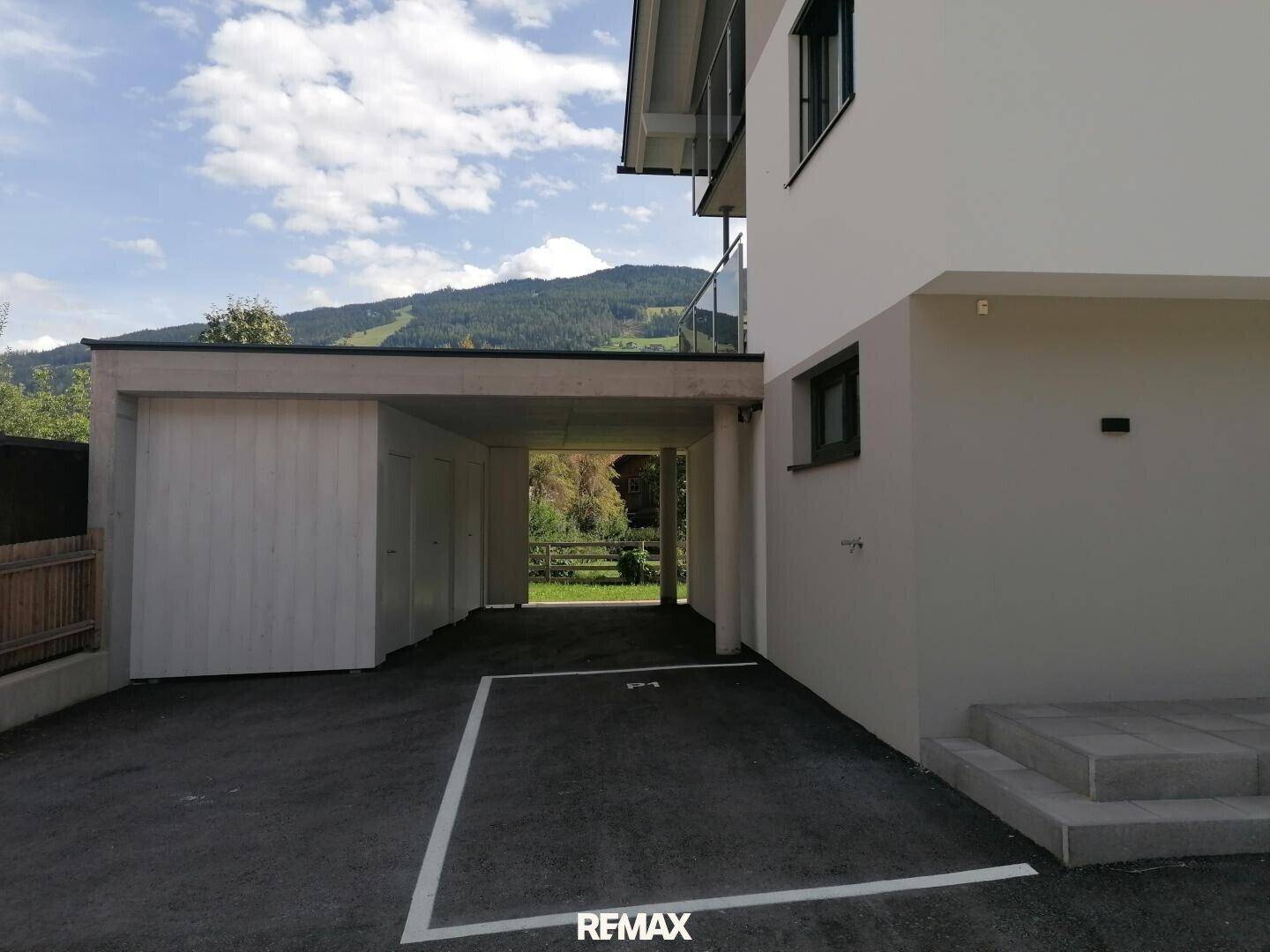 Außenansicht des Gebäudes mit einem Carport und einem markierten Parkplatz im Vordergrund.