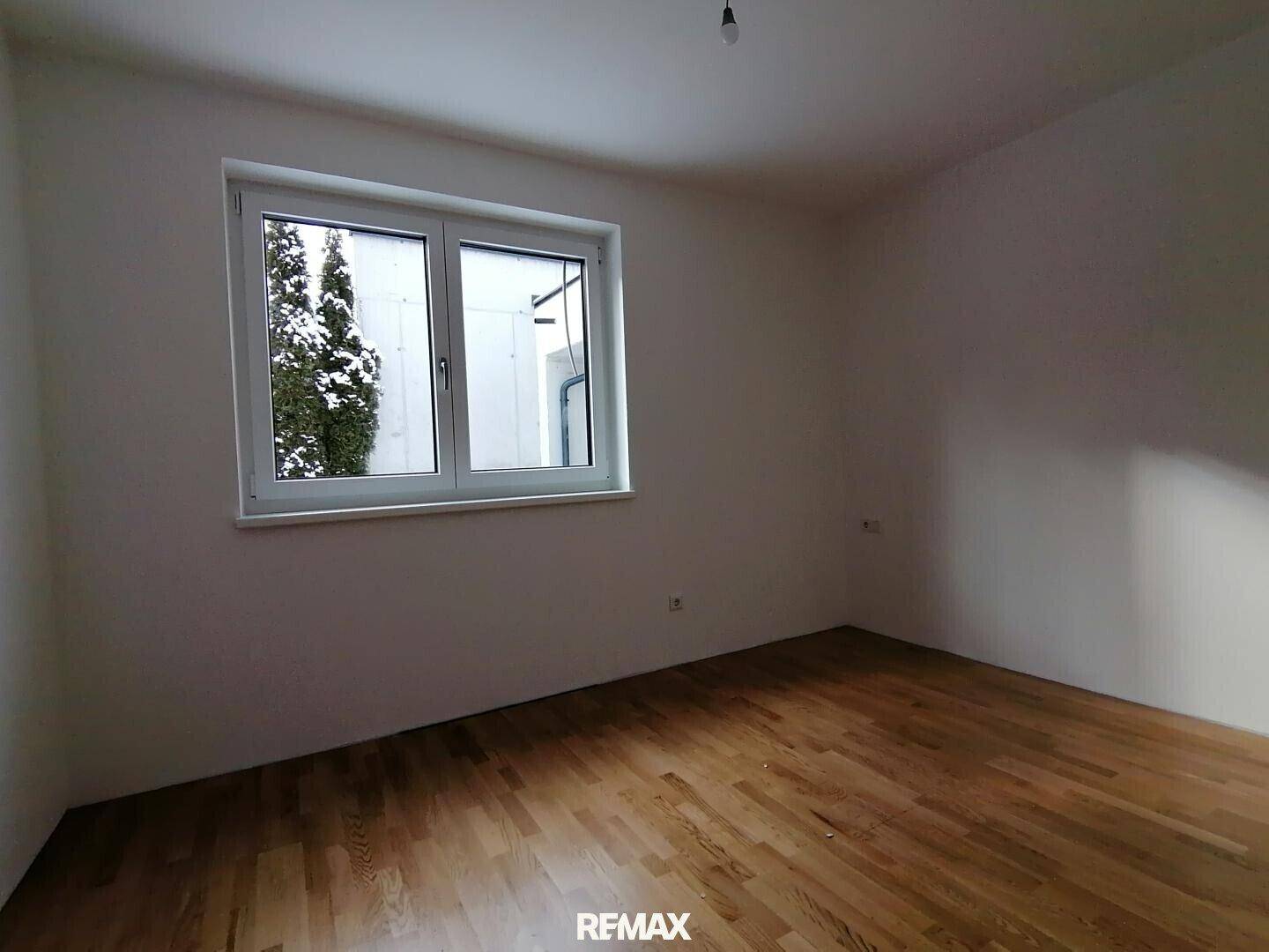 Leeres Schlafzimmer mit Parkettboden und Fenster, das einen Blick nach draußen bietet.