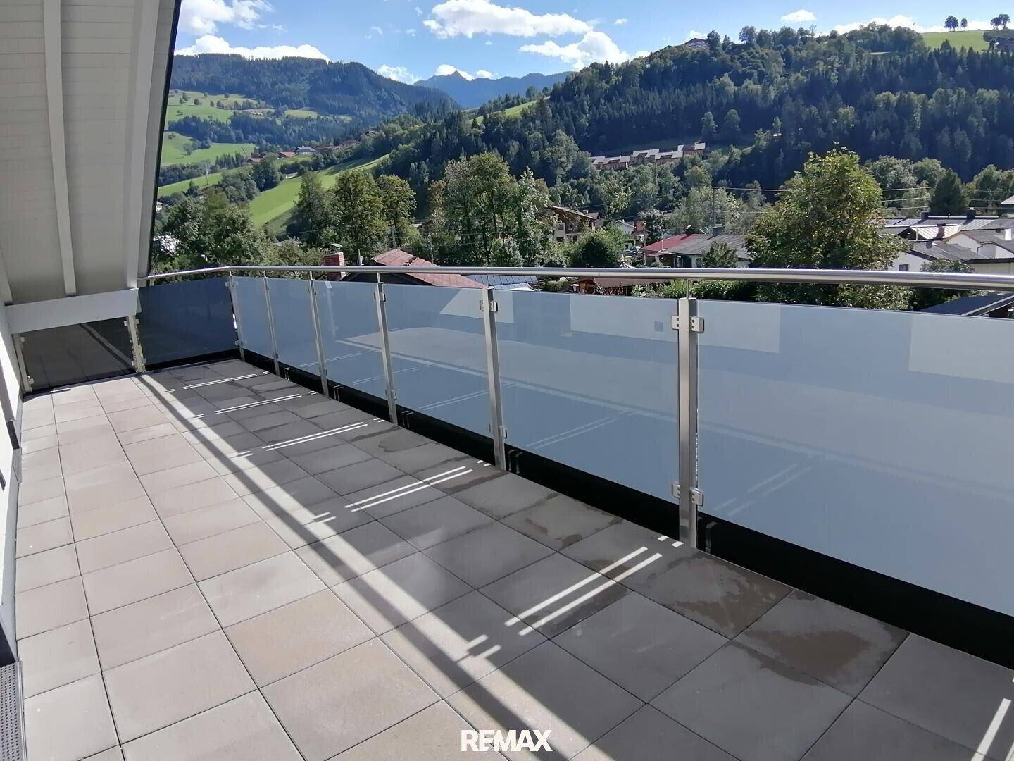 Moderner Balkon mit Glasgeländer und Fliesenboden, bietet einen weiten Blick auf die Berge.
