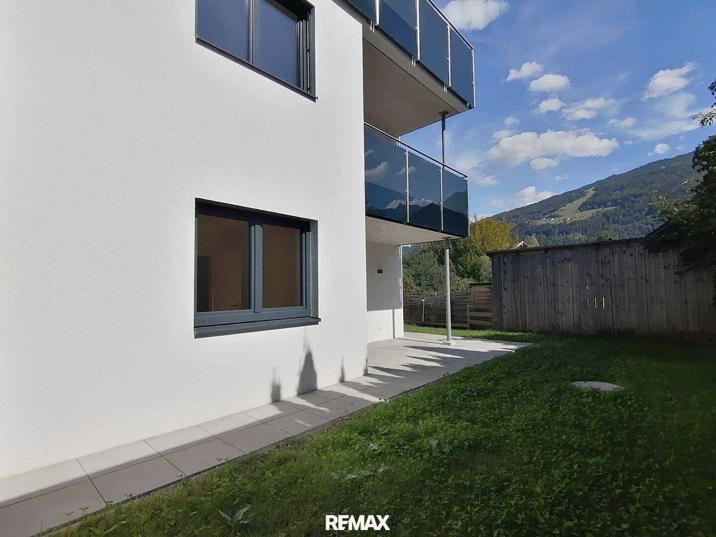 Seitenansicht des Gebäudes mit Rasenfläche und Zugang zu einer kleinen Terrasse.