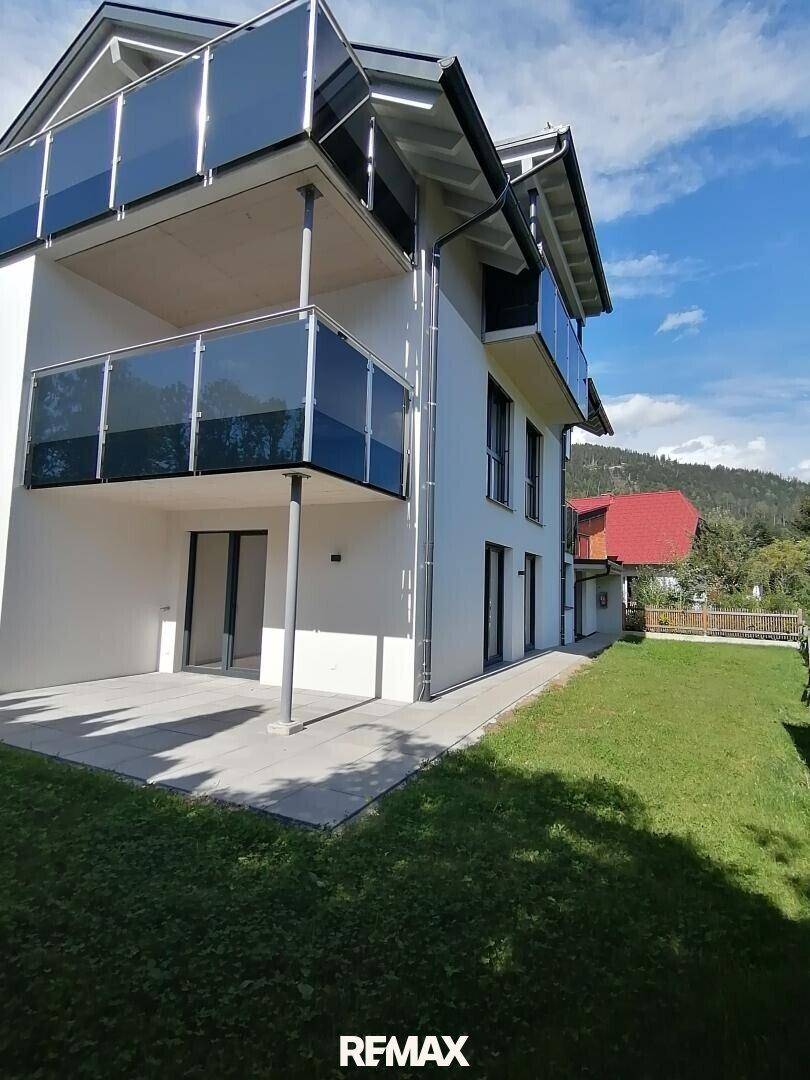 Neubau mit mehreren Balkonen und einer weitläufigen Rasenfläche im sonnigen Außenbereich.