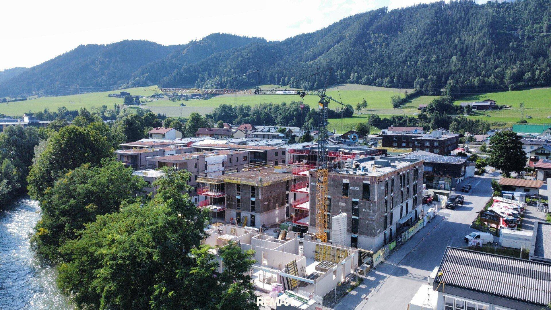 Luftaufnahme von Gebäuden im Bau am Flussufer mit Bergen im Hintergrund.