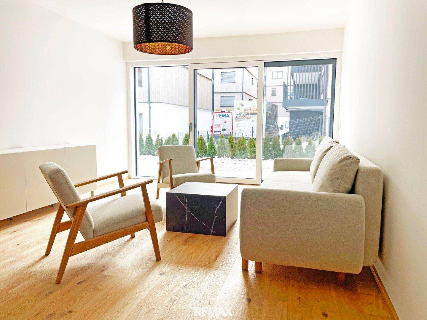 Helles Wohnzimmer mit beigem Sofa, Sesseln und großen Schiebetüren zum Außenbereich.