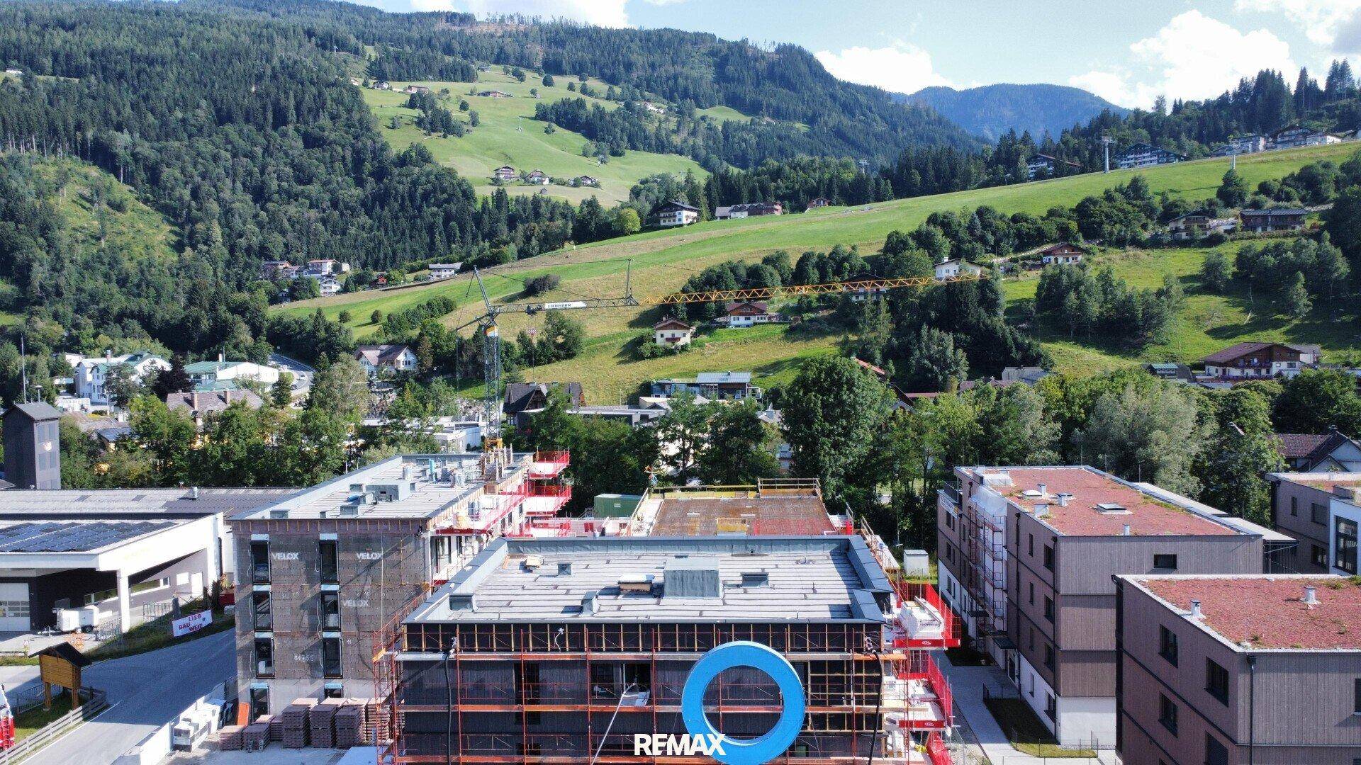 Luftaufnahme einer Baustelle mit neuen Gebäuden in einer grünen Berglandschaft.