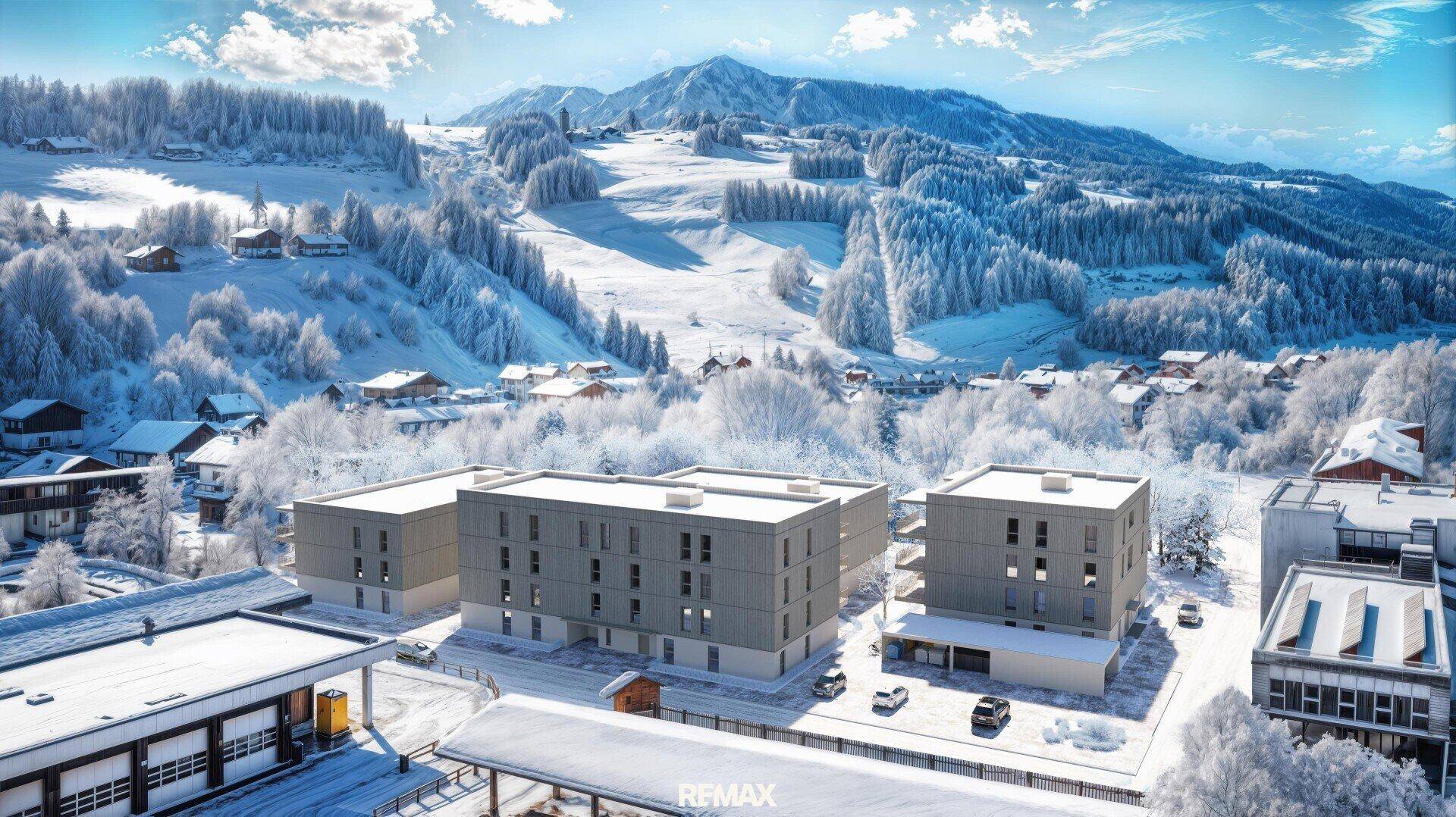 Winterliche Luftaufnahme von modernen Gebäuden in einer verschneiten Berglandschaft mit vielen Bäumen.