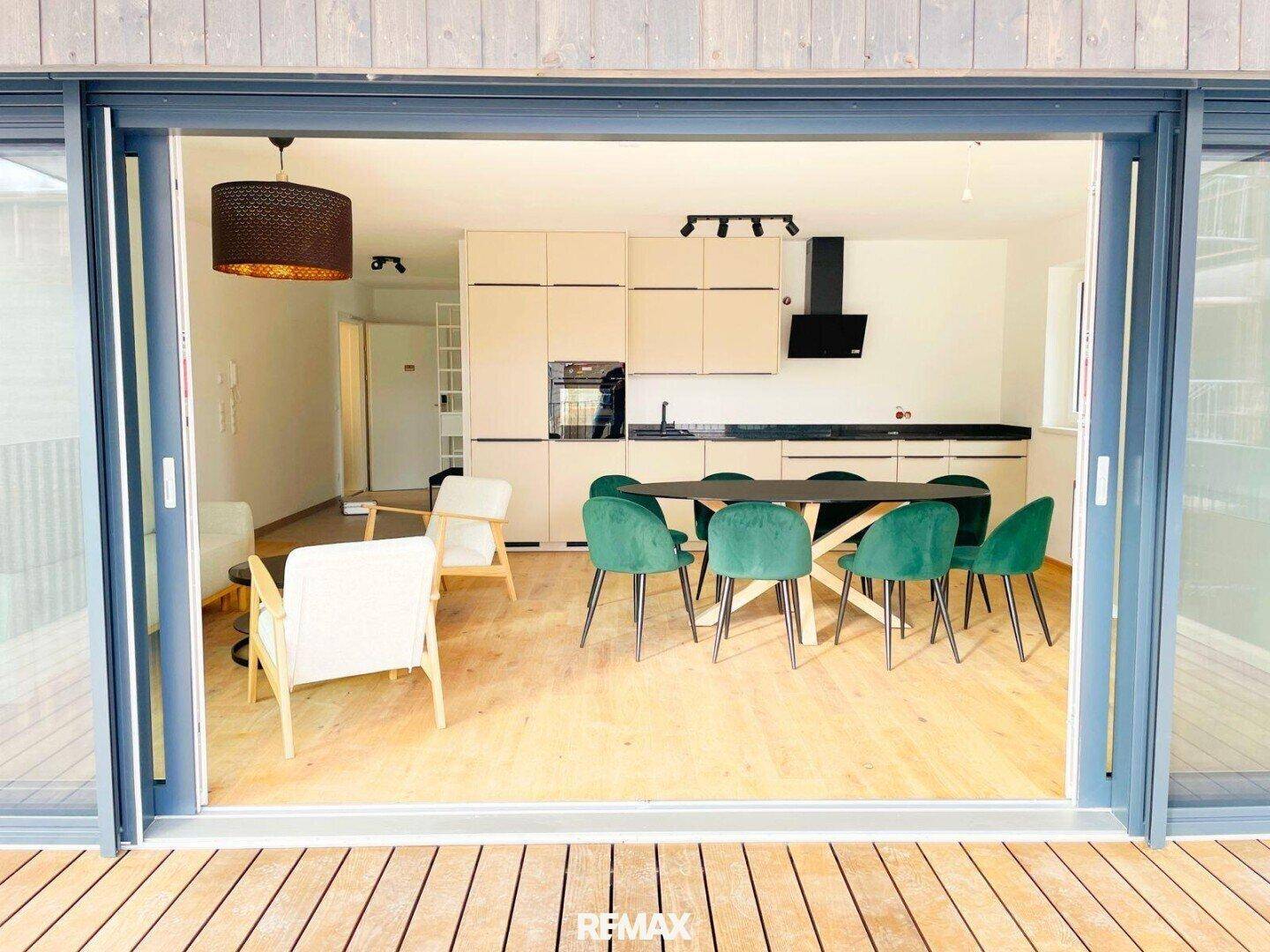 Offener Wohn-Essbereich mit moderner Küche und großem Schiebetürzugang zu einer Holzterrasse.