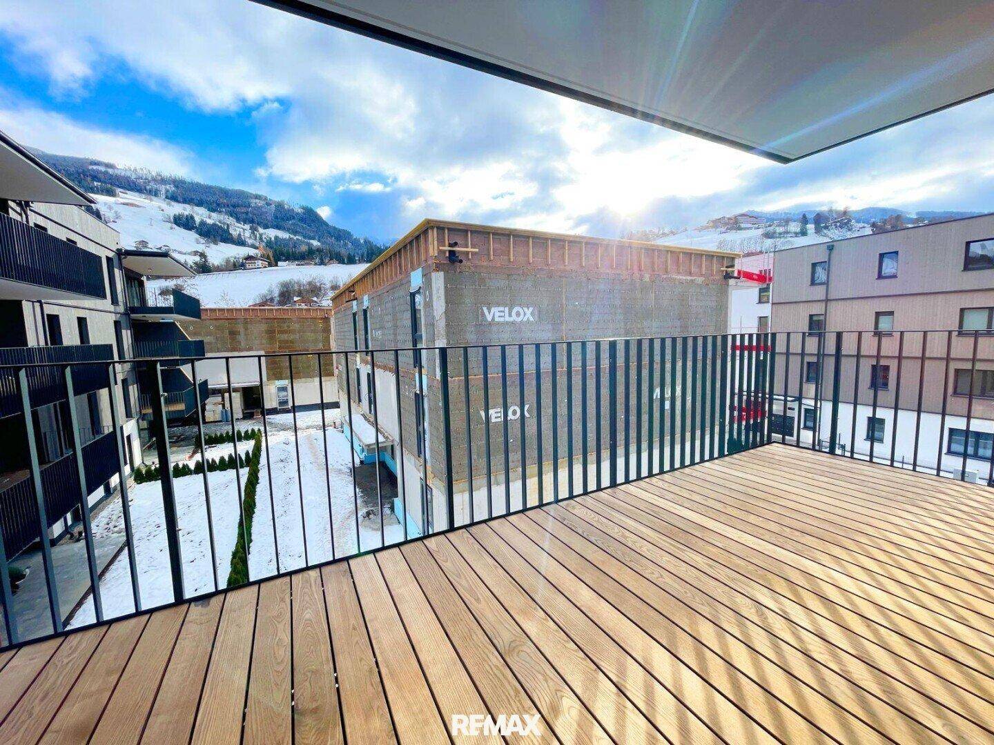Geräumiger Balkon mit Holzboden und Blick auf die umliegende Berglandschaft und eine Baustelle.