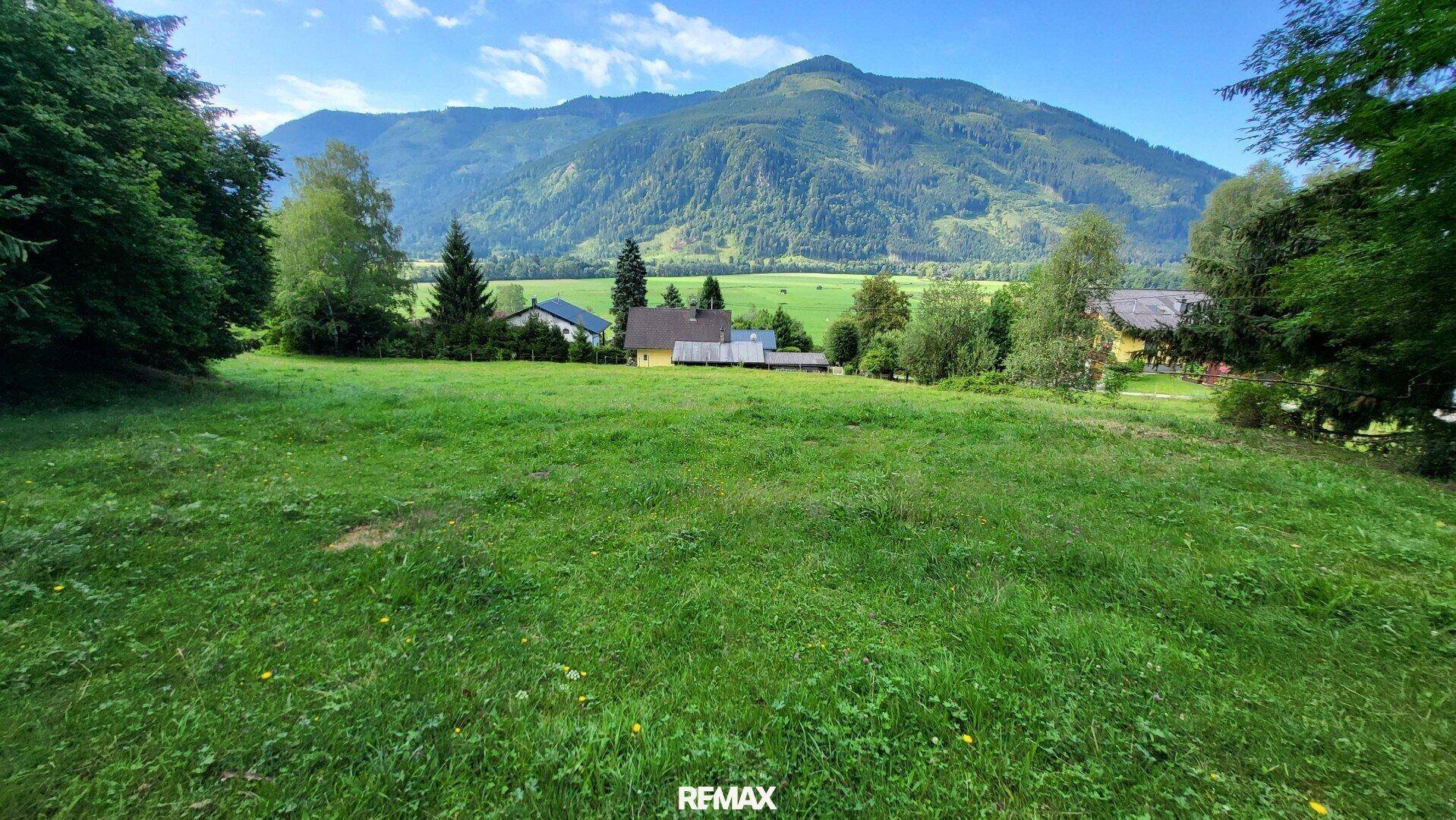 Idyllische Wiesenlandschaft mit Häusern im Hintergrund und beeindruckendem Bergblick.