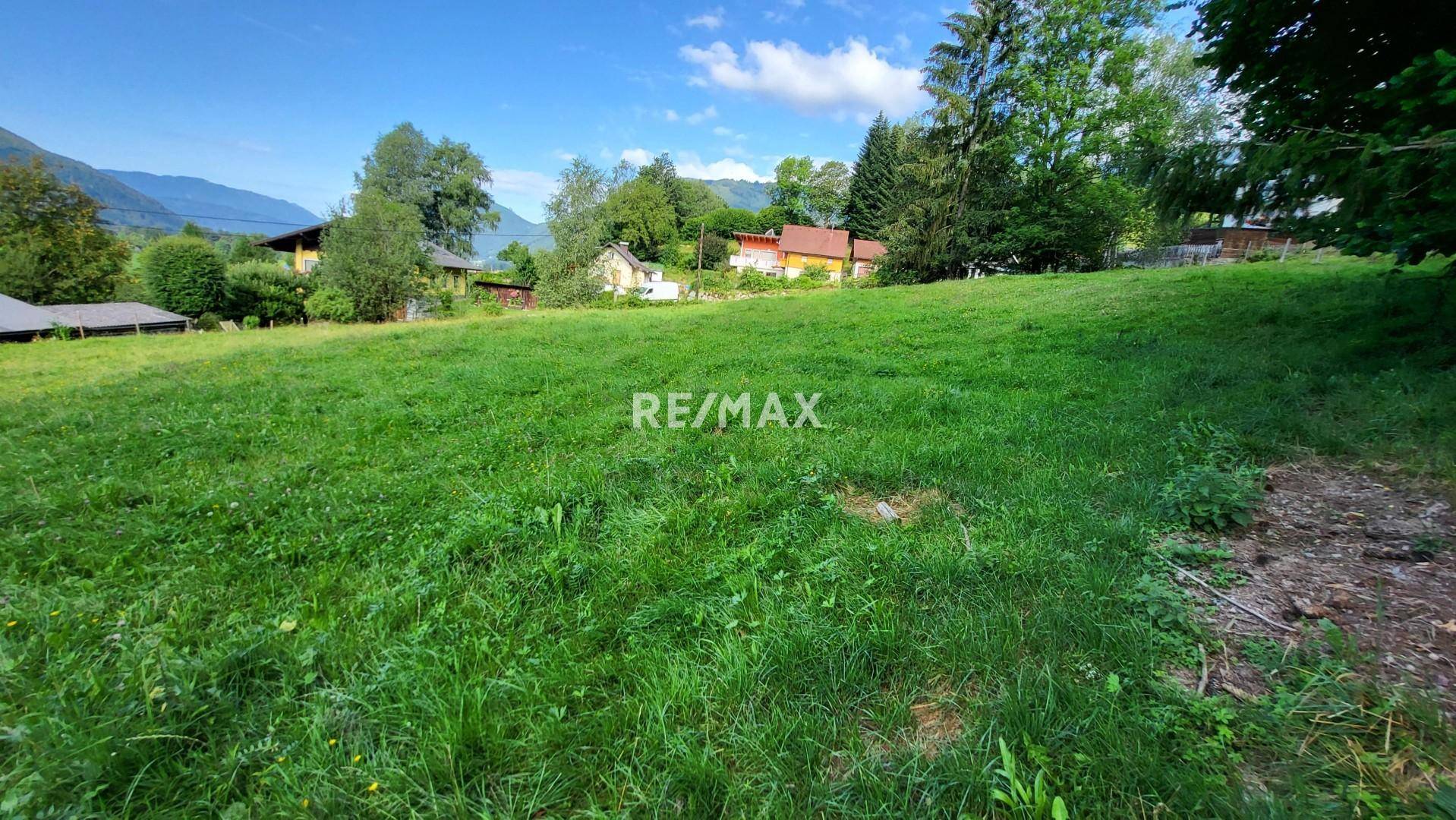 Idyllische Wiesenlandschaft mit Blick auf bewaldete Hügel und vereinzelte Häuser.