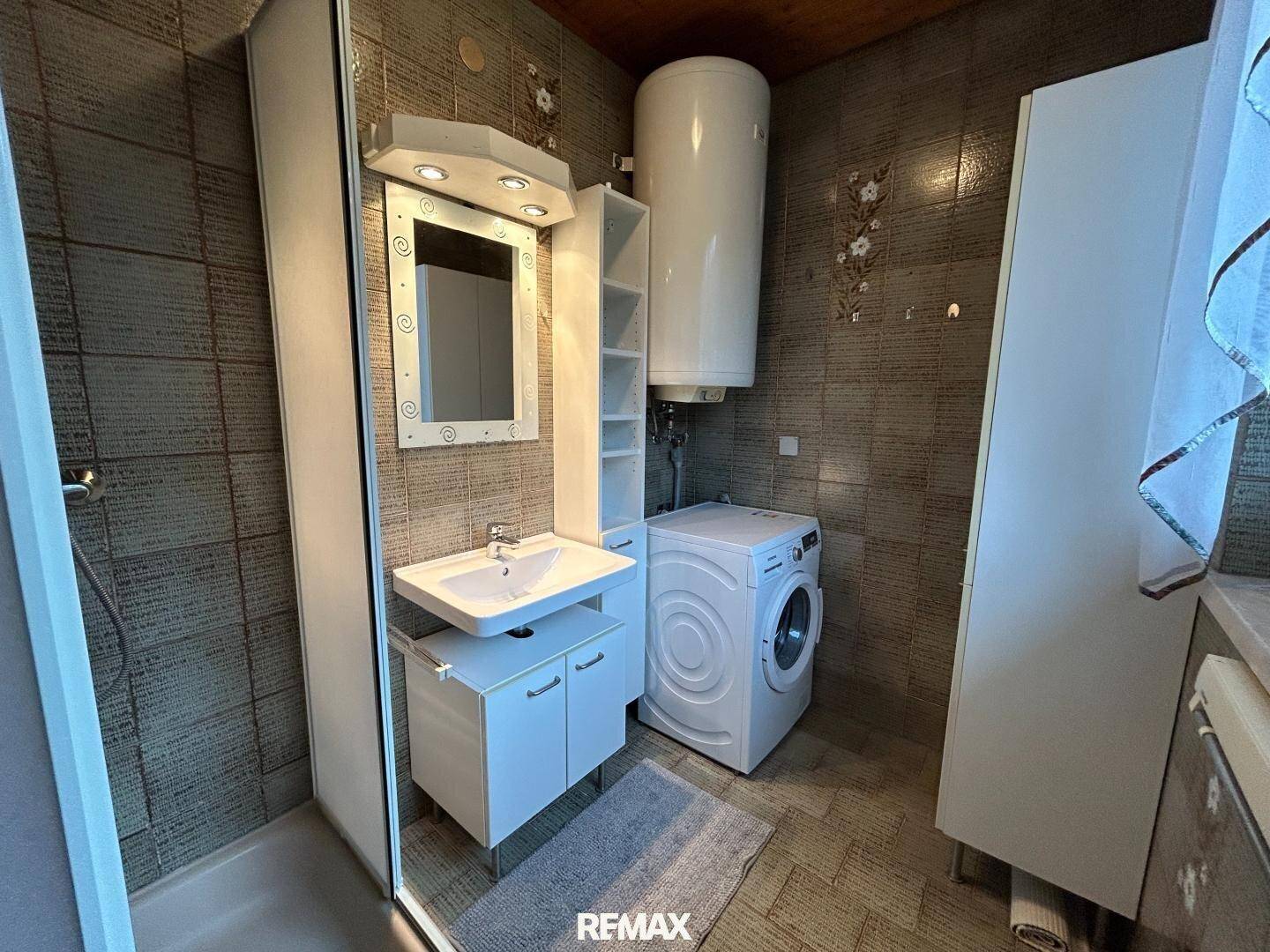 Badezimmer mit Waschmaschine, Warmwasserboiler, Einzelwaschbecken und Spiegelschrank.