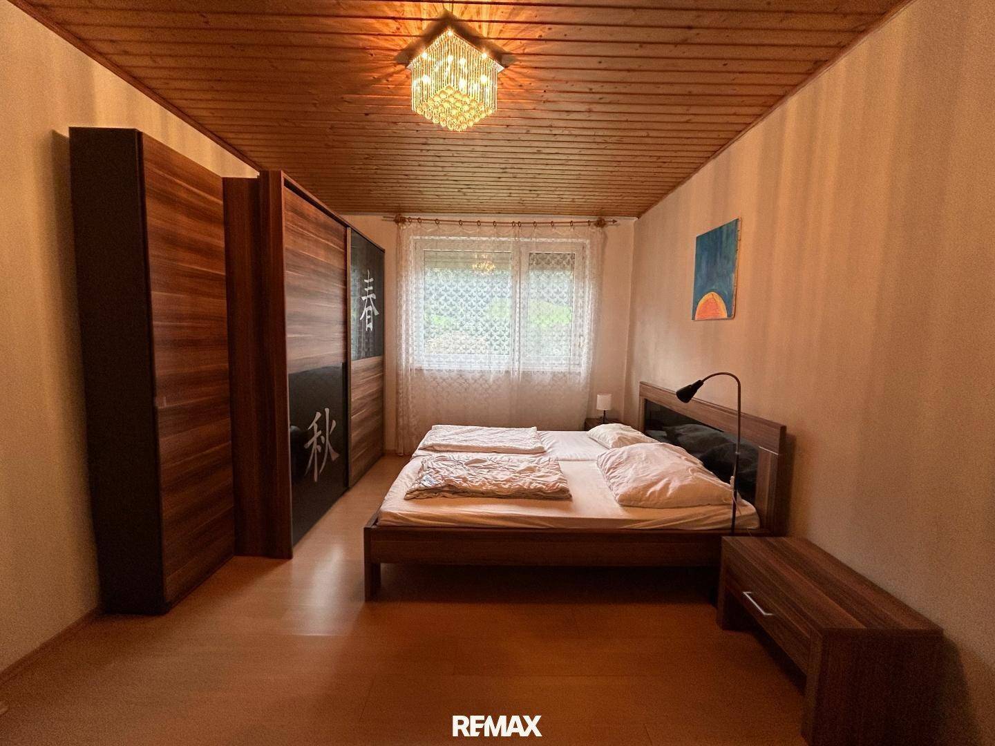 Helles Schlafzimmer mit Doppelbett, Holzdecke und einem großen Schrank mit Schiebetüren.