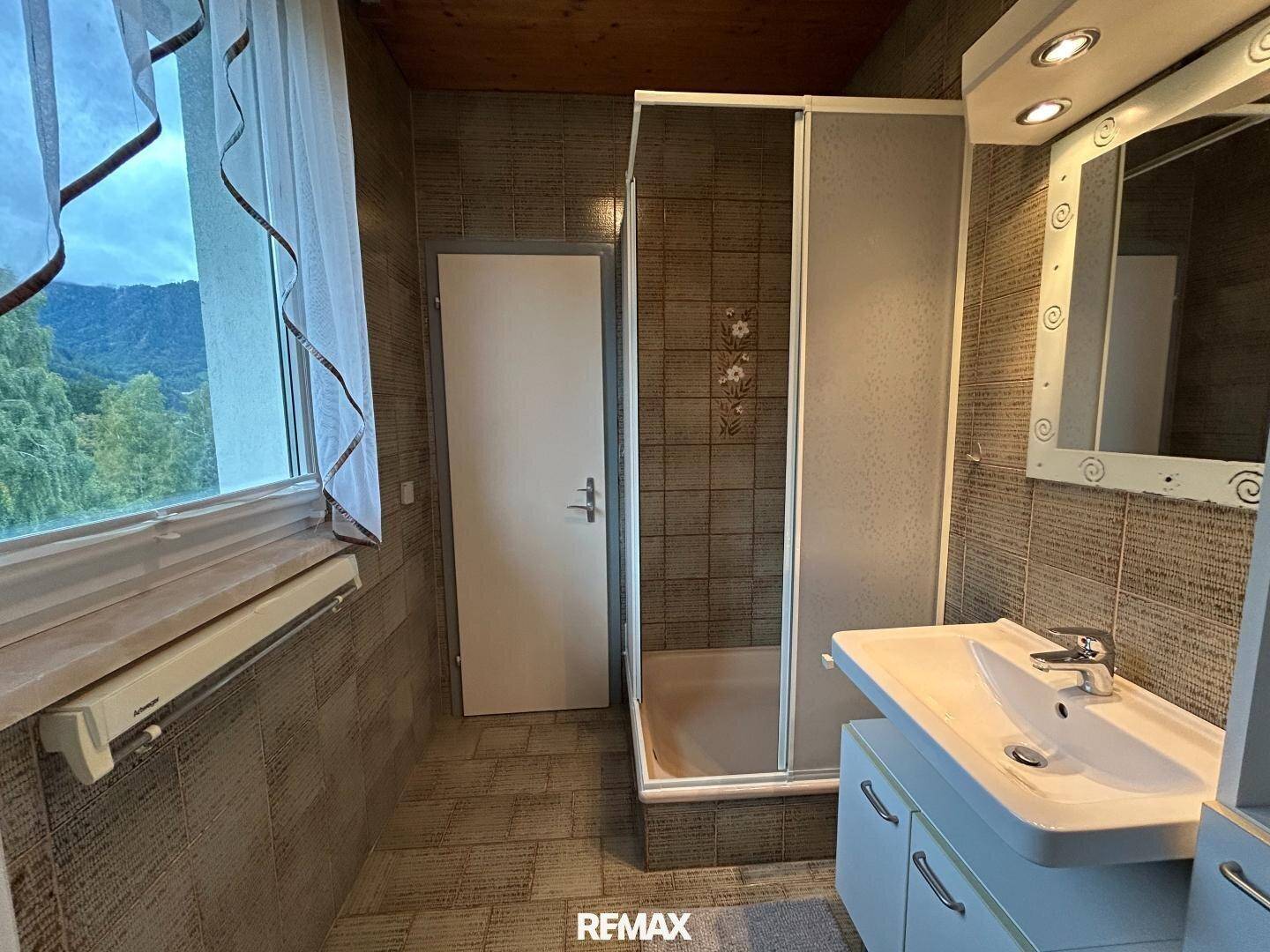 Badezimmer mit Fliesen, Duschkabine, Einzelwaschbecken und einem Fenster mit Bergblick.
