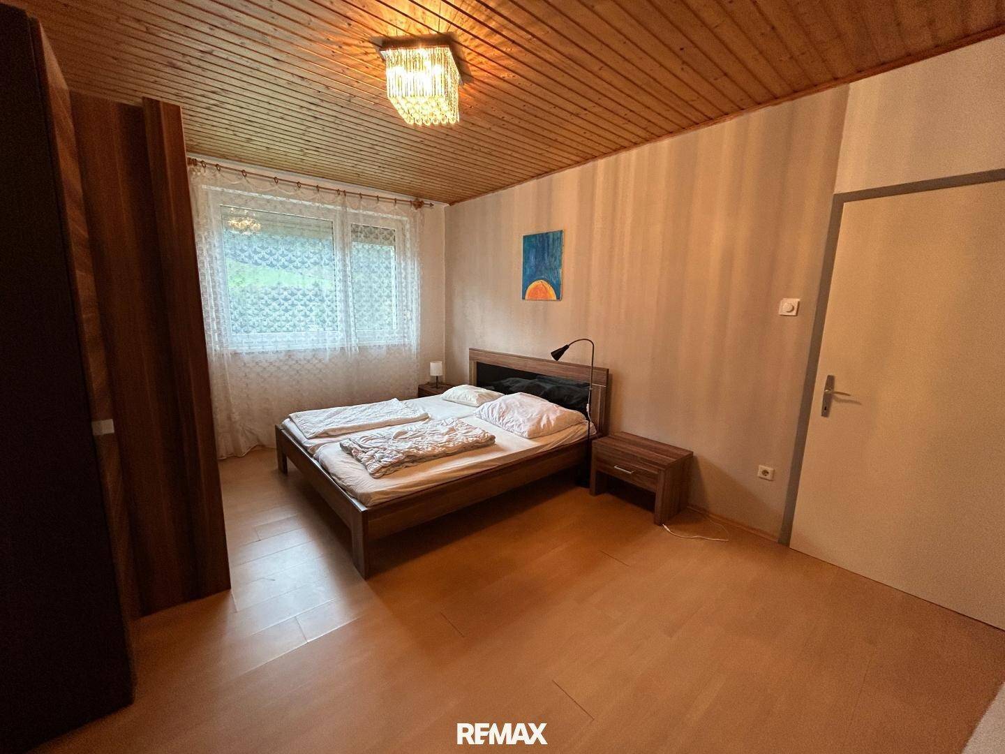 Schlafzimmer mit Doppelbett, Holztäfeldecke, Laminatboden und Fenster mit Blick ins Grüne.
