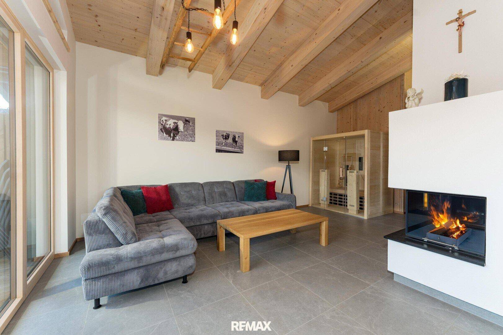 Heller Wohnbereich mit Kamin, Holzbalkendecke und integrierter Sauna für Wellnessmomente.