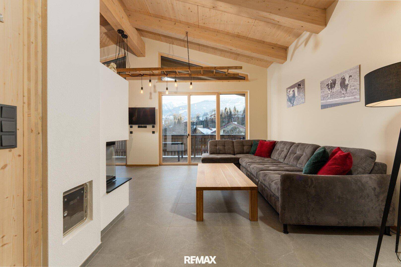 Gemütliches Wohnzimmer mit großem Sofa, Kamin und weitem Blick auf die Berge.